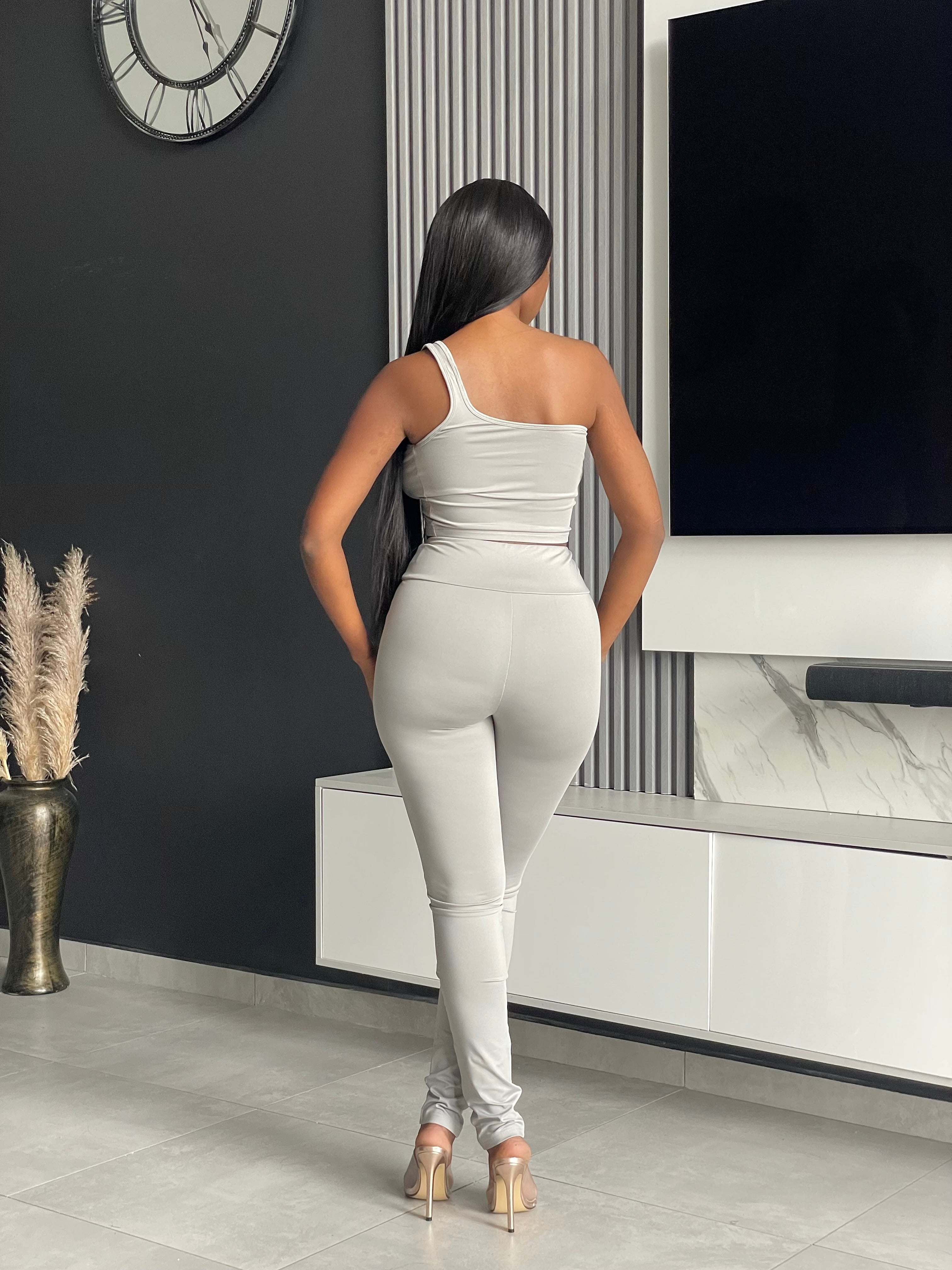 Model wearing the Ama Pant Set in light grey, featuring a one-shoulder crop top and jogger-style pants with drawstring.