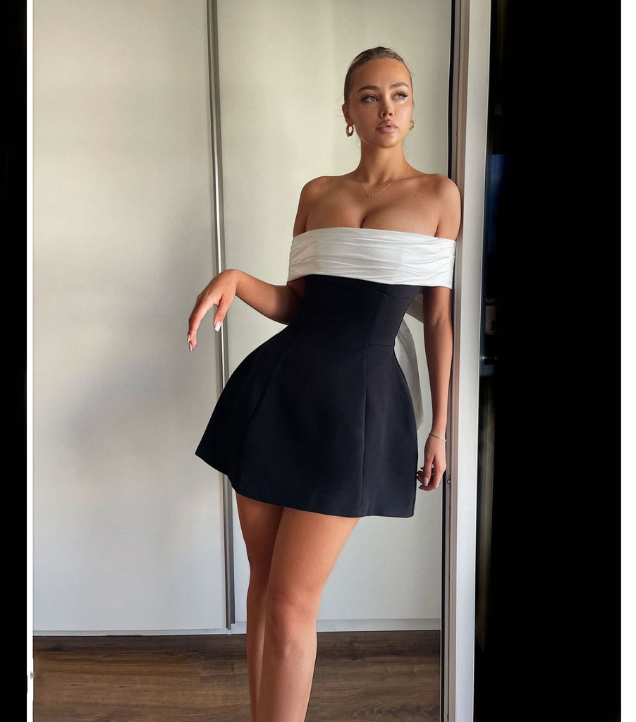 Woman wearing the Lila Bow-Back Mini Dress featuring an oversized satin bow, off-shoulder neckline, and a chic black and white design.