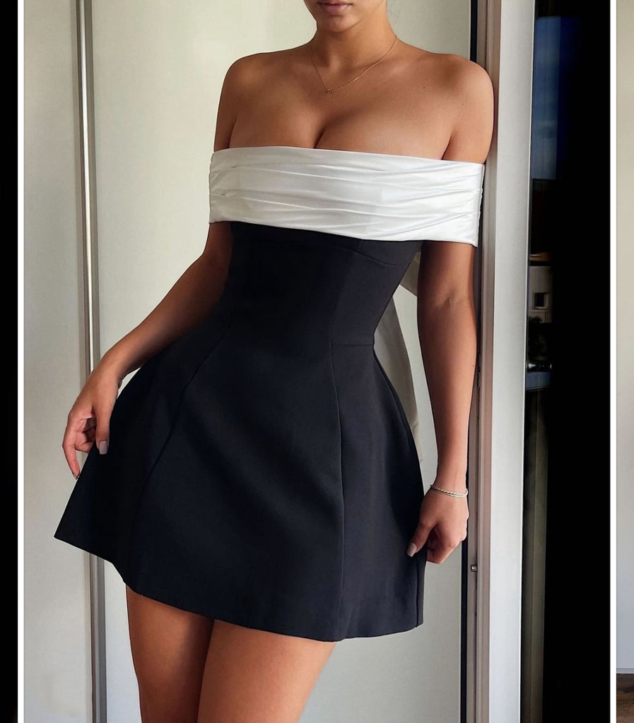 Woman wearing the Lila Bow-Back Mini Dress featuring an oversized satin bow, off-shoulder neckline, and a chic black and white design.