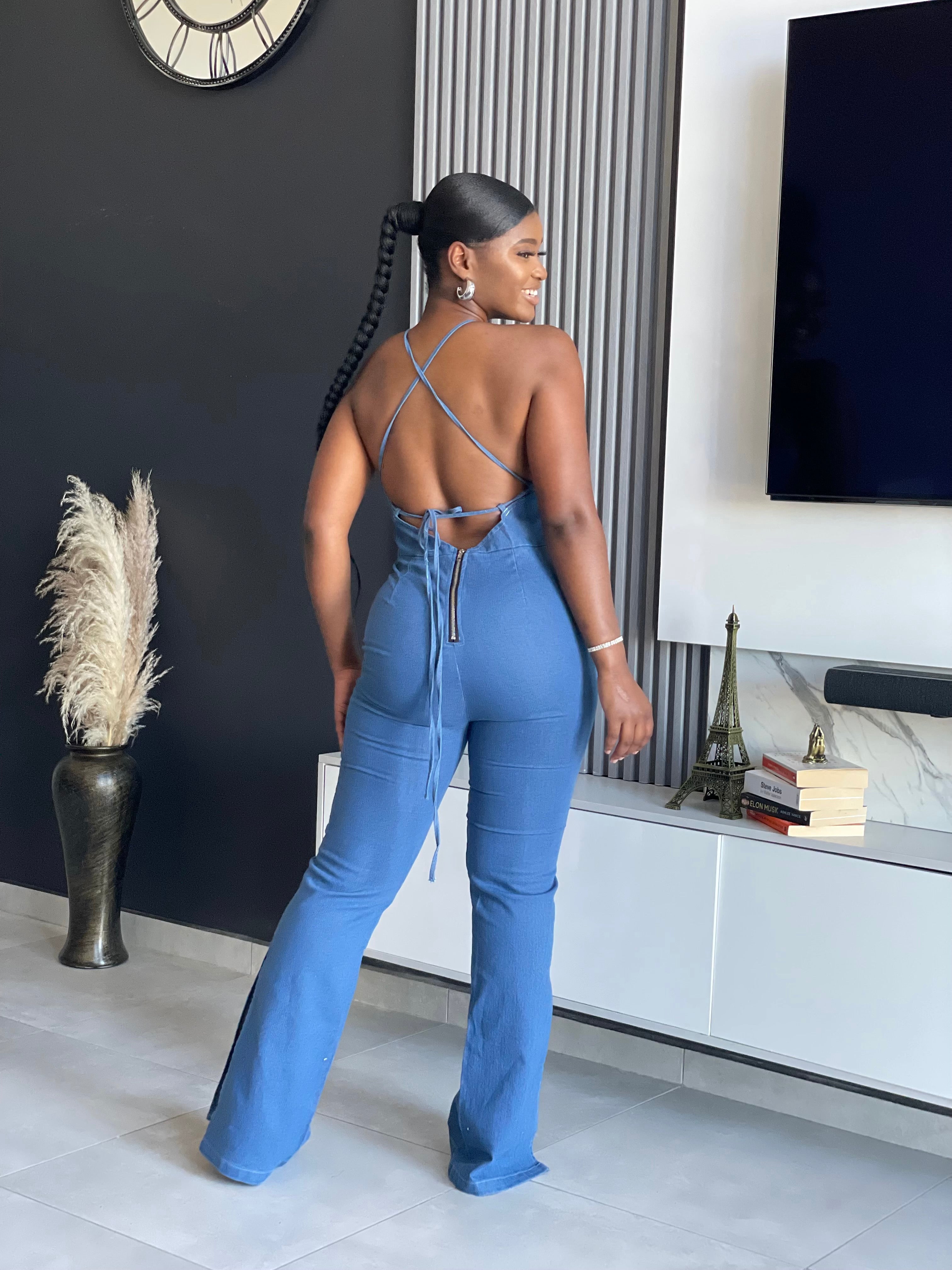 A woman wearing the ‘ SetThe Trend Denim Jumpsuit’ with a halter top and flared legs, showcasing a stretchy, comfortable fit, ideal for fashionable outings.