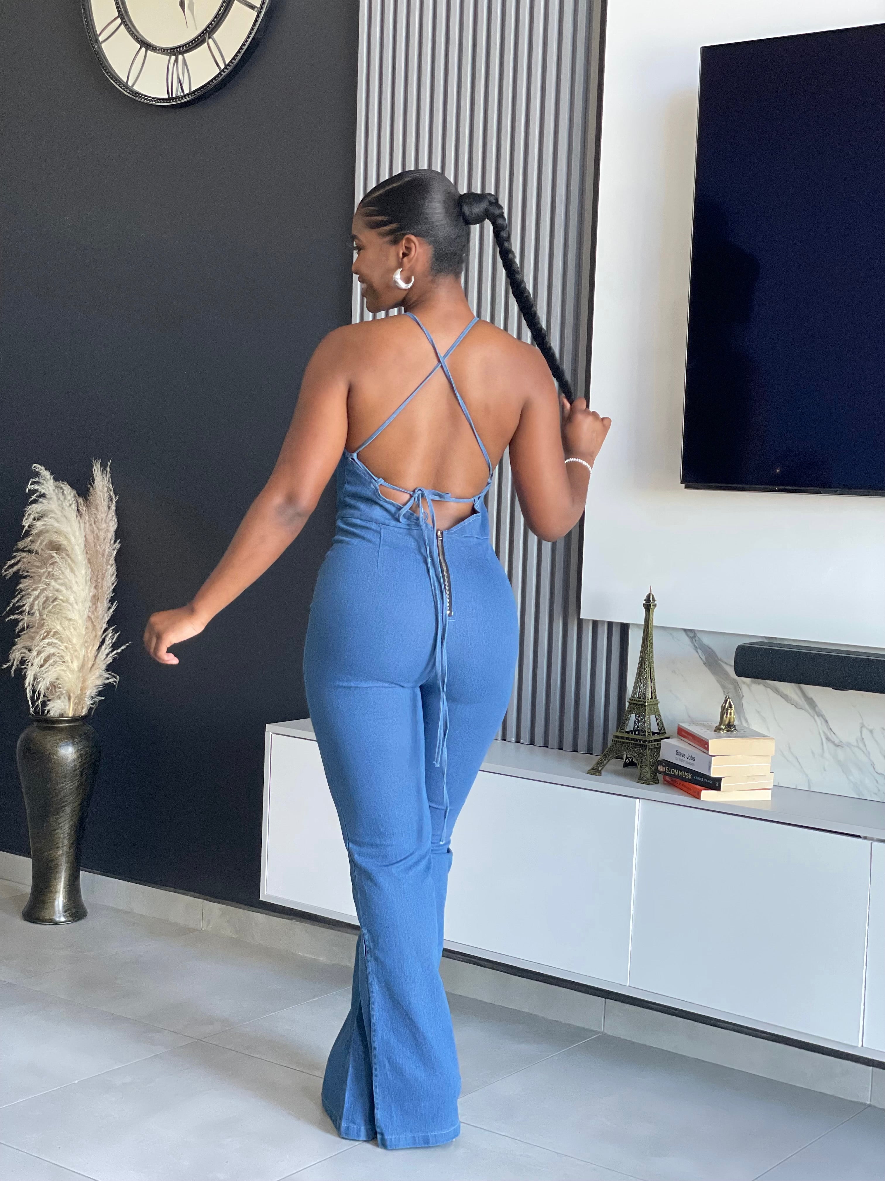 A woman wearing the ‘ SetThe Trend Denim Jumpsuit’ with a halter top and flared legs, showcasing a stretchy, comfortable fit, ideal for fashionable outings.