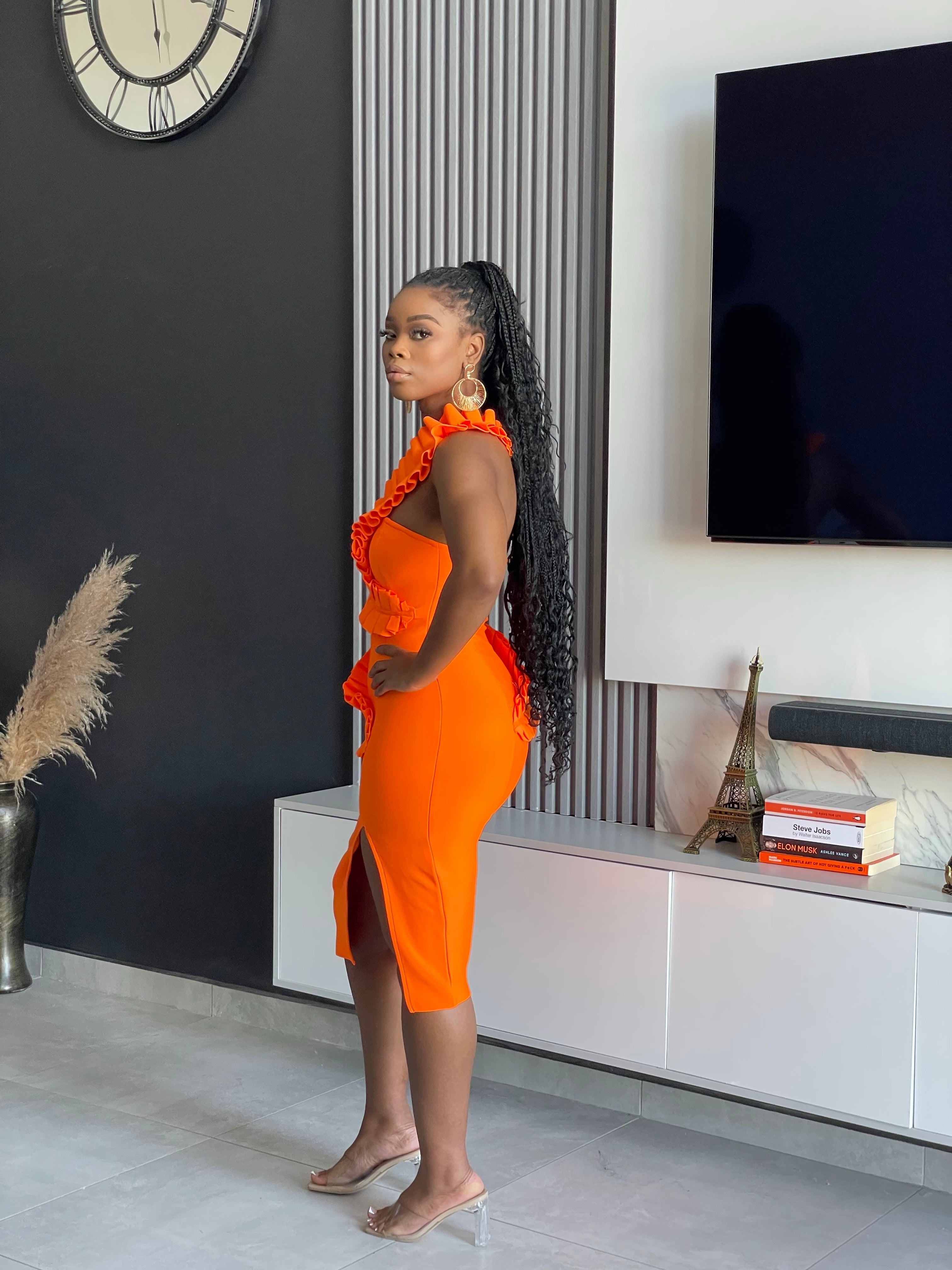 A woman in an XS size Breath Taking Bandage Midi Dress in vibrant orange with ruffle detailing, ideal for special occasions