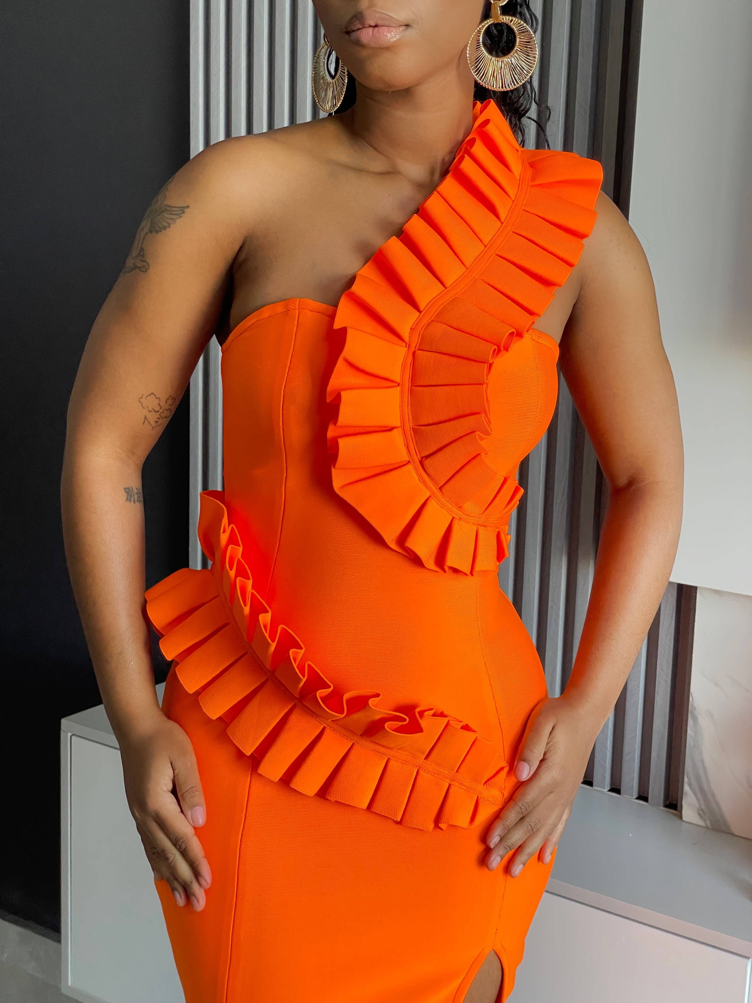 A woman in an XS size Breath Taking Bandage Midi Dress in vibrant orange with ruffle detailing, ideal for special occasions