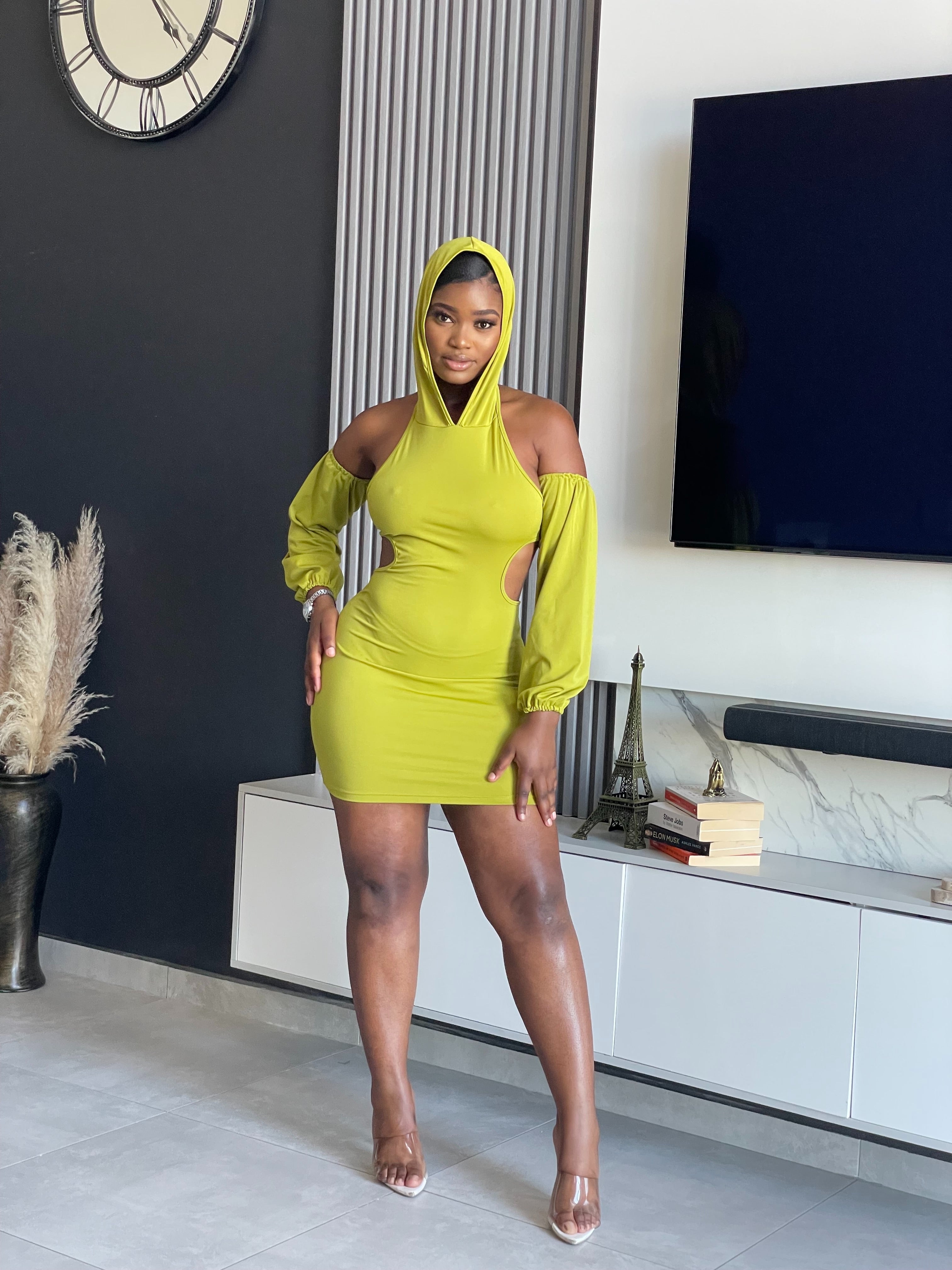 A woman in a Simmina Mini Dress in lime green with hood and cut-out details, standing confidently, perfect for stylish outings