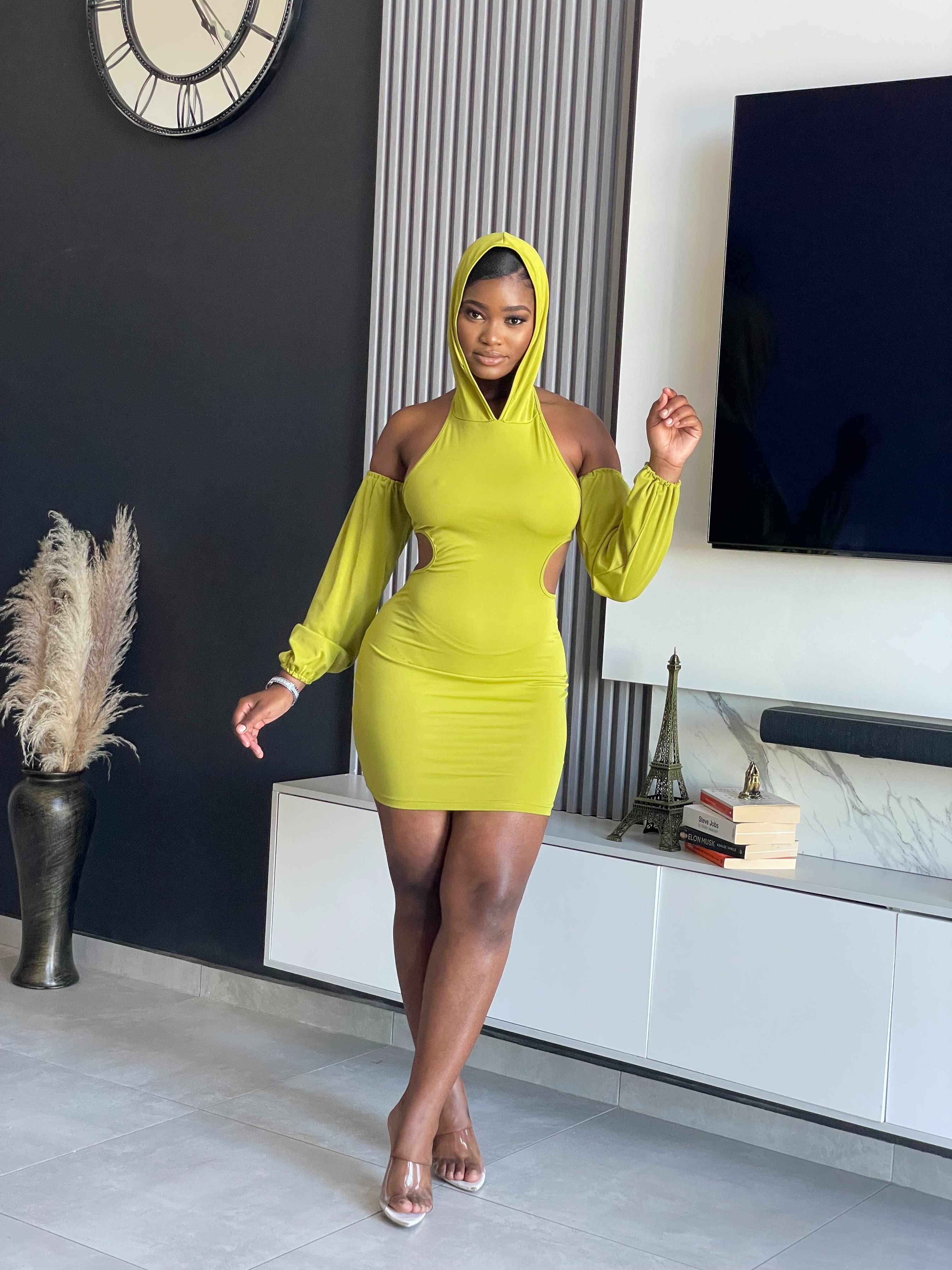 A woman in a Simmina Mini Dress in lime green with hood and cut-out details, standing confidently, perfect for stylish outings