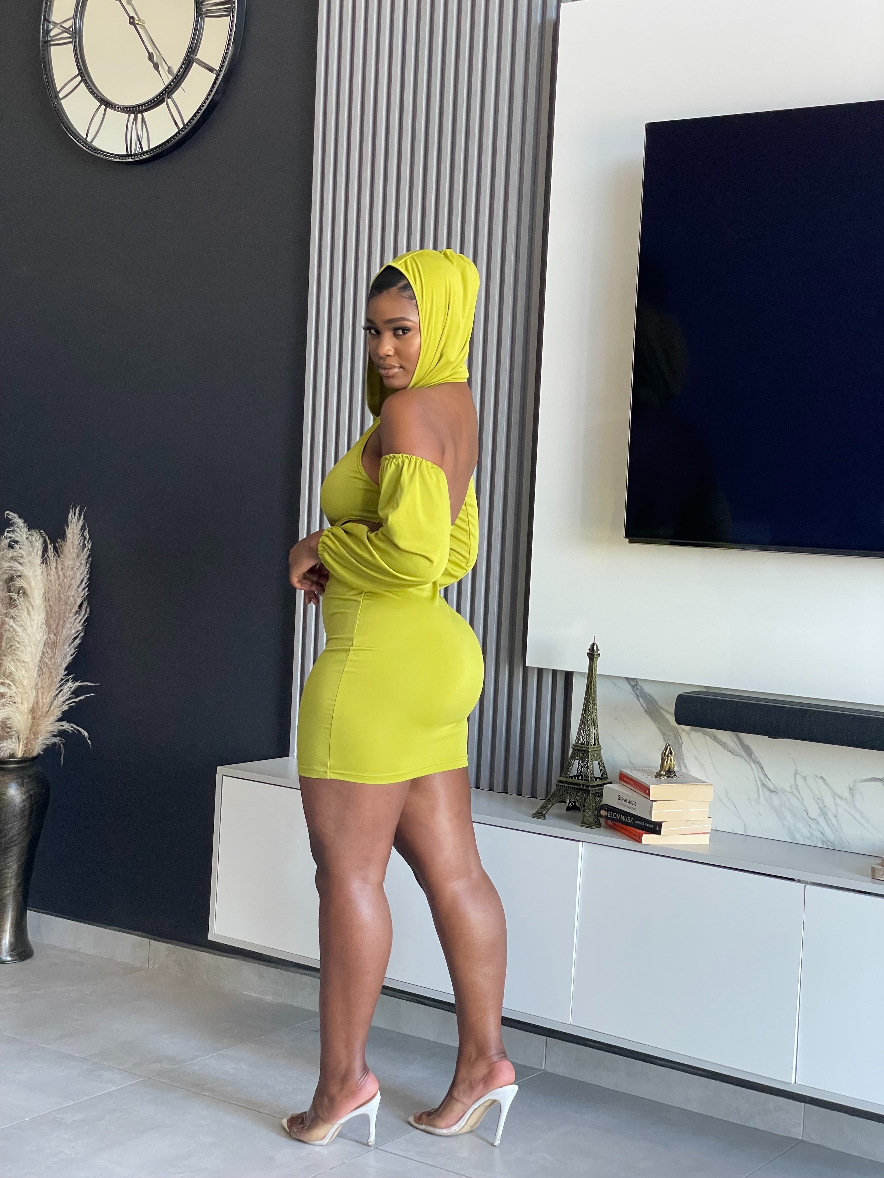 A woman in a Simmina Mini Dress in lime green with hood and cut-out details, standing confidently, perfect for stylish outings