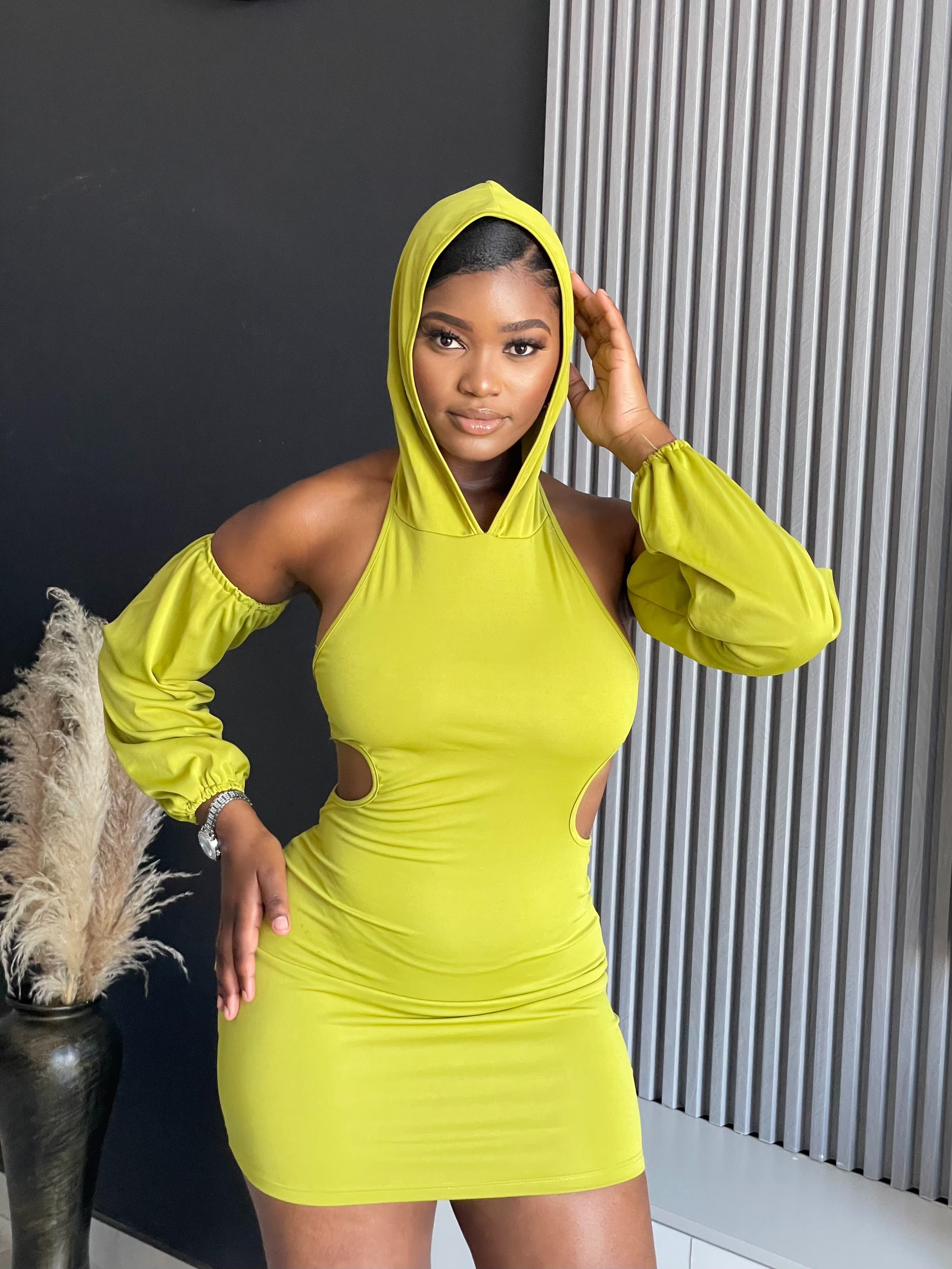 A woman in a Simmina Mini Dress in lime green with hood and cut-out details, standing confidently, perfect for stylish outings