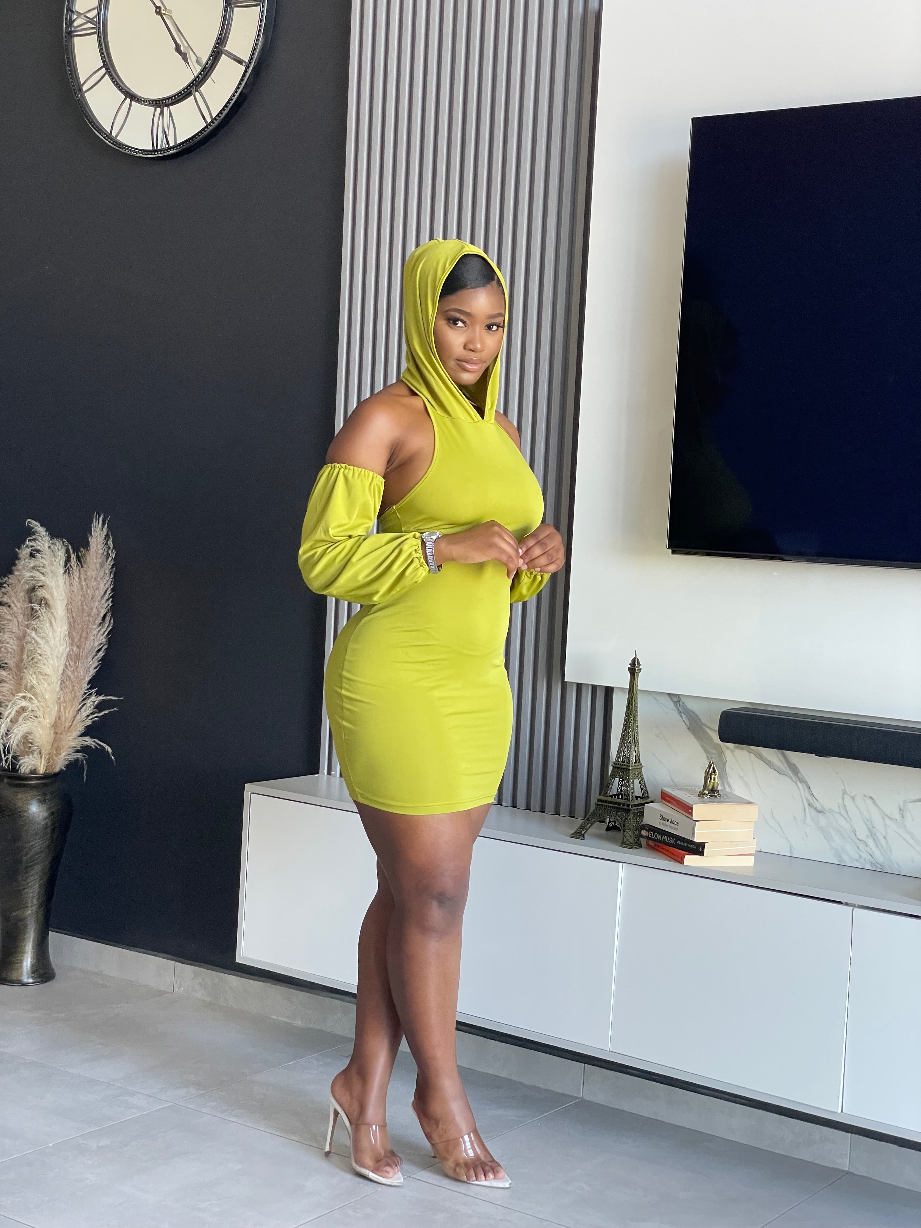 A woman in a Simmina Mini Dress in lime green with hood and cut-out details, standing confidently, perfect for stylish outings