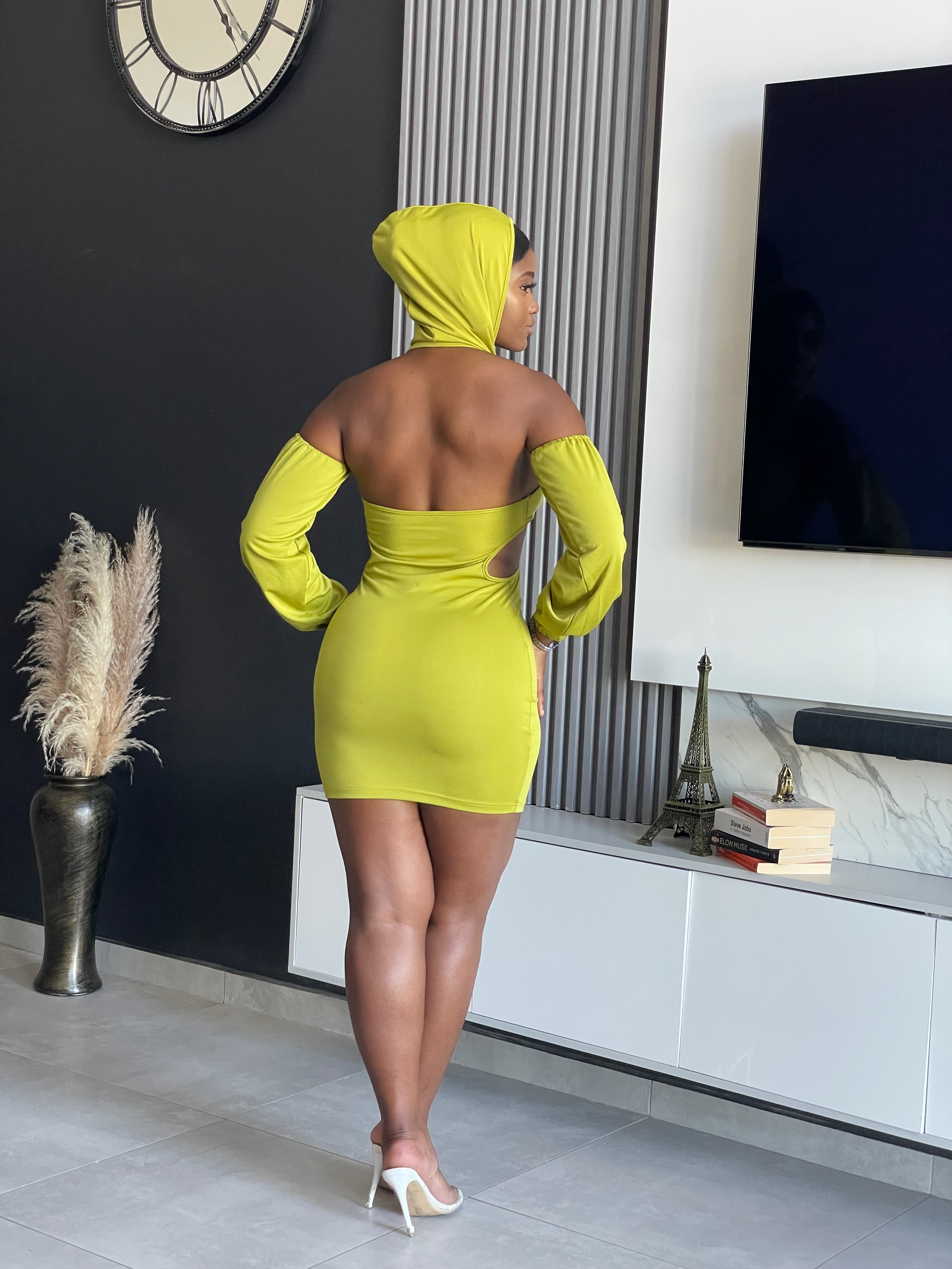 A woman in a Simmina Mini Dress in lime green with hood and cut-out details, standing confidently, perfect for stylish outings