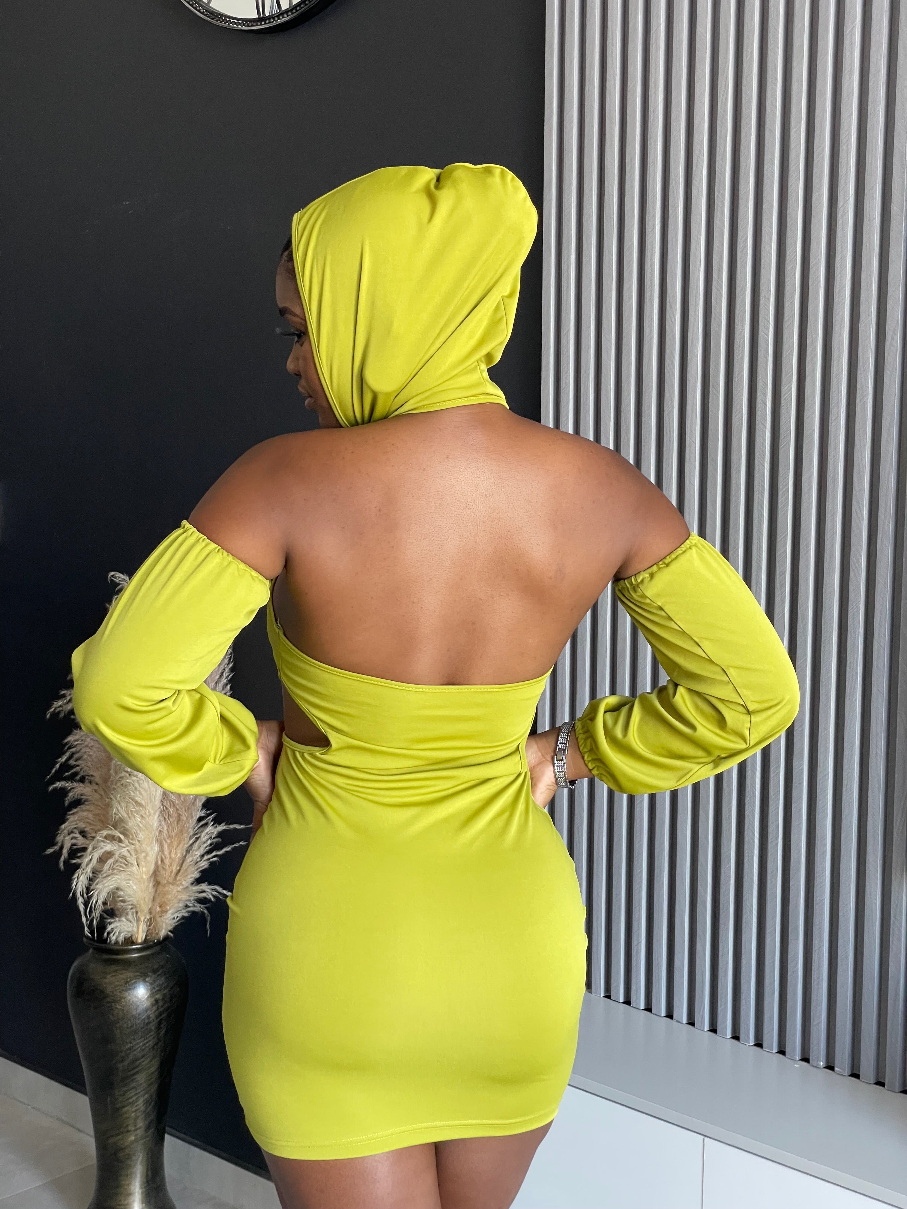 A woman in a Simmina Mini Dress in lime green with hood and cut-out details, standing confidently, perfect for stylish outings