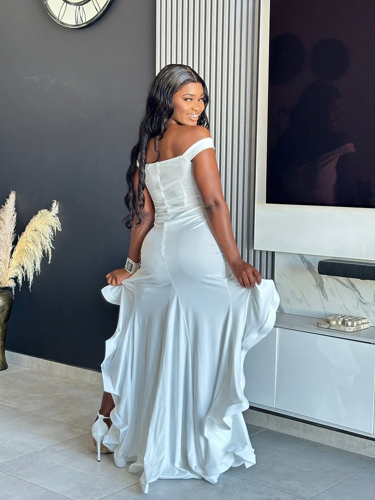 Model wearing It’s Giving Maxi Dress in white, featuring an off-shoulder design and ruffled hem, perfect for formal events.