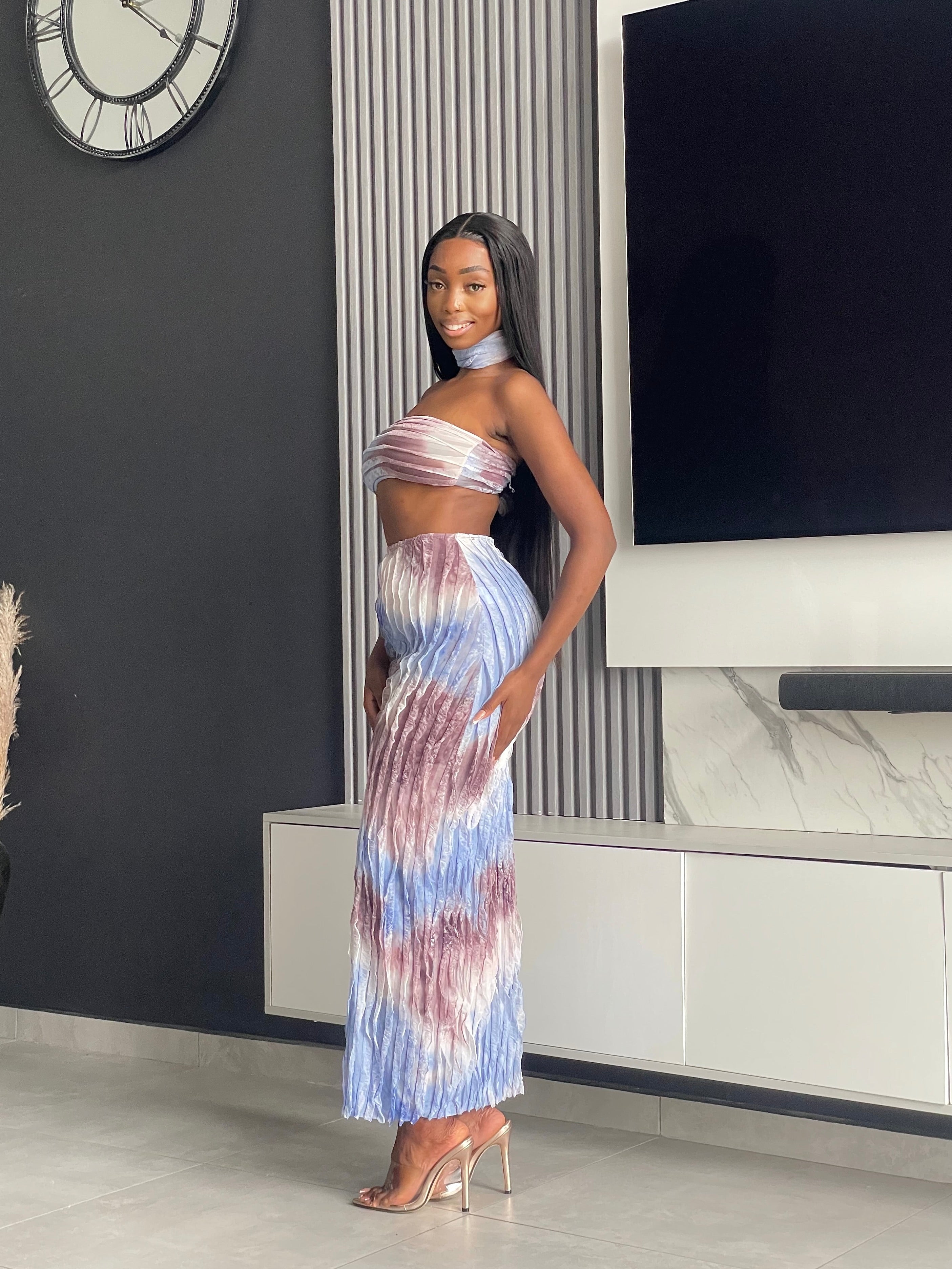 Model wearing the Tana Skirt Set, a tie-dye two-piece outfit with a strapless bandeau top, pleated maxi skirt, and matching neckpiece.