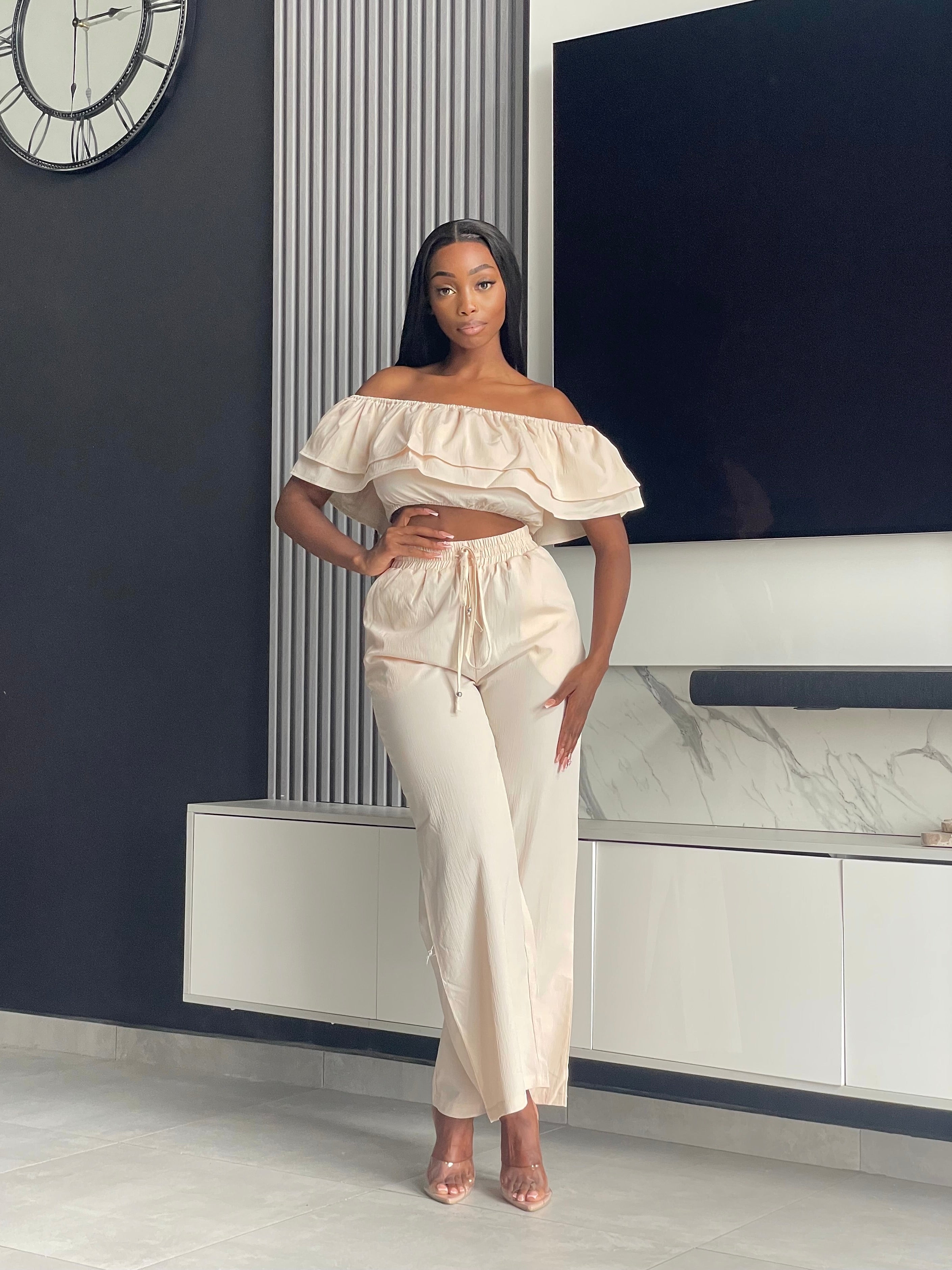 Model wearing the Varouna Pant Set in beige, featuring an off-shoulder ruffled crop top and wide-leg pants, perfect for casual outings.