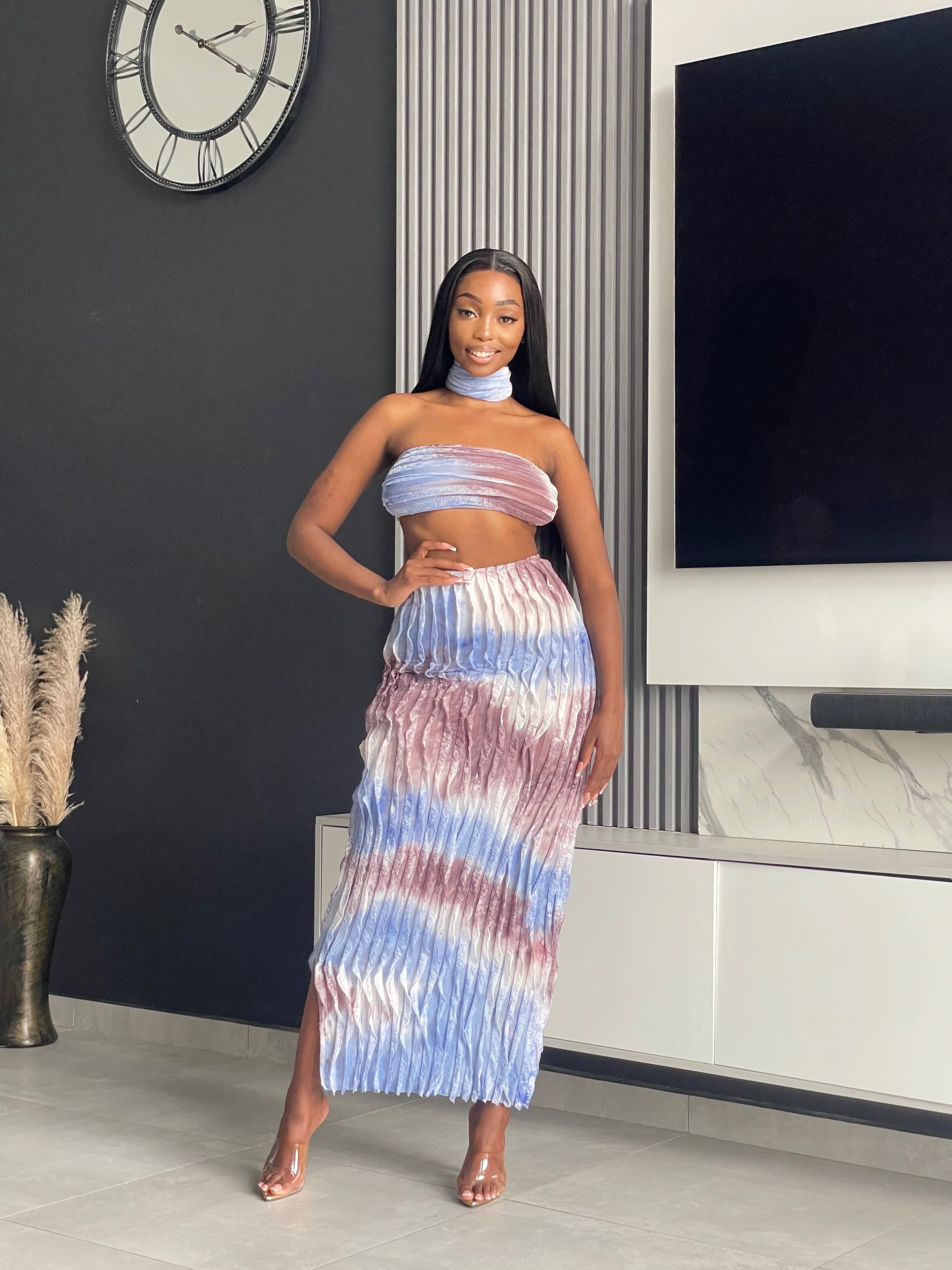 Model wearing the Tana Skirt Set, a tie-dye two-piece outfit with a strapless bandeau top, pleated maxi skirt, and matching neckpiece.