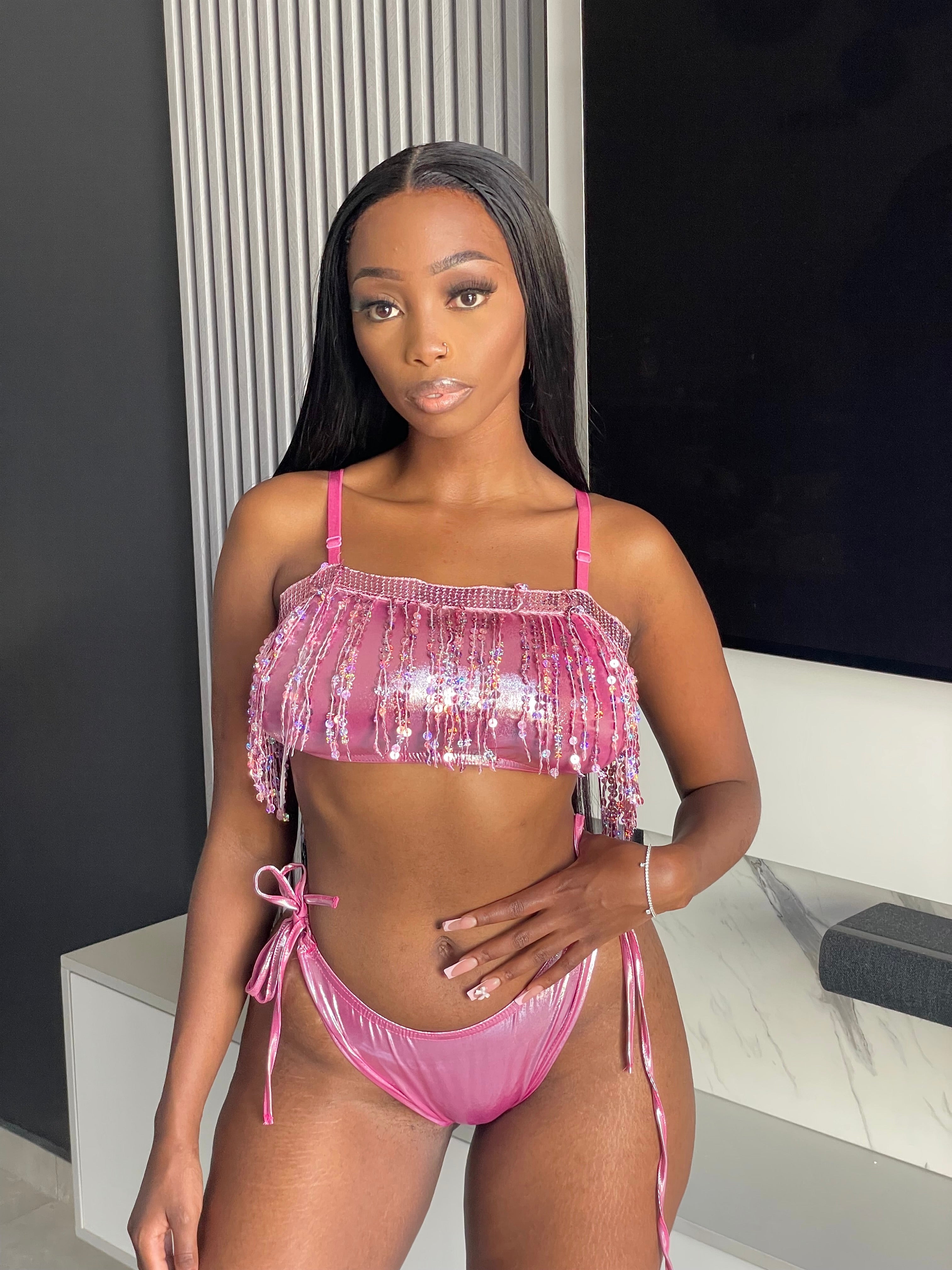 Model wearing the Auja Bikini, a pink sequin two-piece set featuring a fringe crop top and adjustable side-tie bottoms, perfect for beach days or poolside glamour.