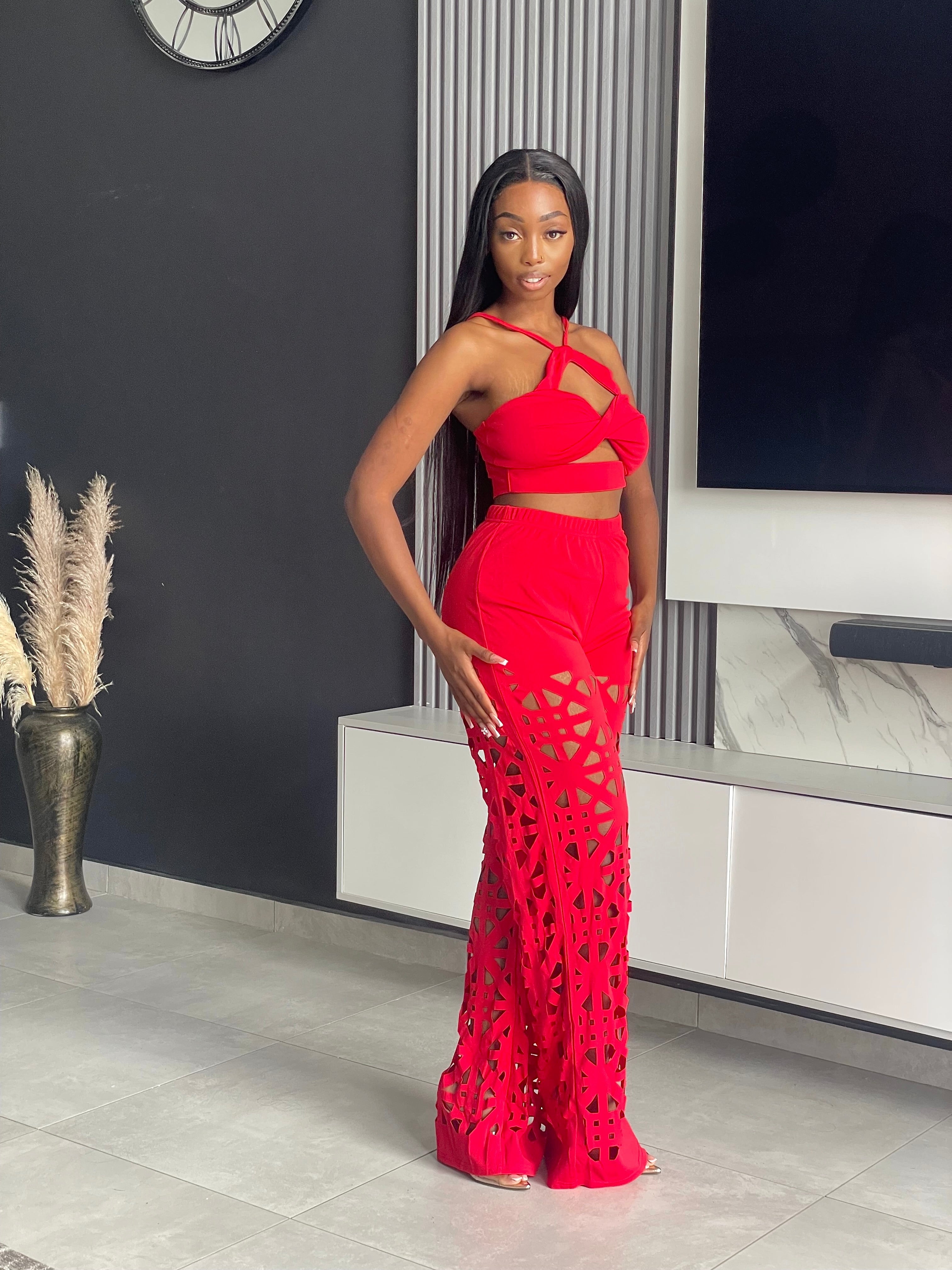 Model wearing the Remedy Pant Set in red, featuring a crisscross halter crop top and wide-leg pants with intricate cutout designs.