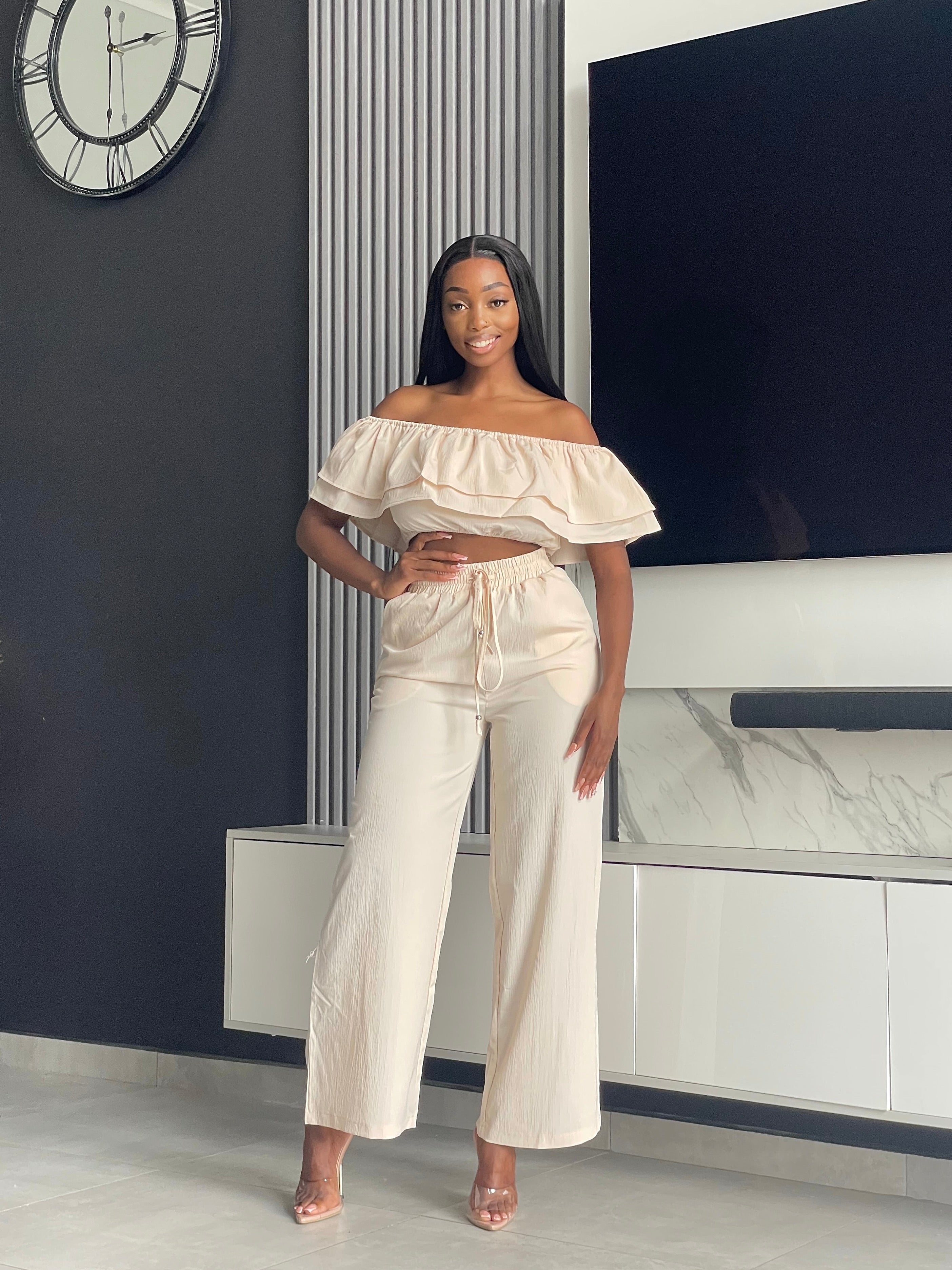 Model wearing the Varouna Pant Set in beige, featuring an off-shoulder ruffled crop top and wide-leg pants, perfect for casual outings.