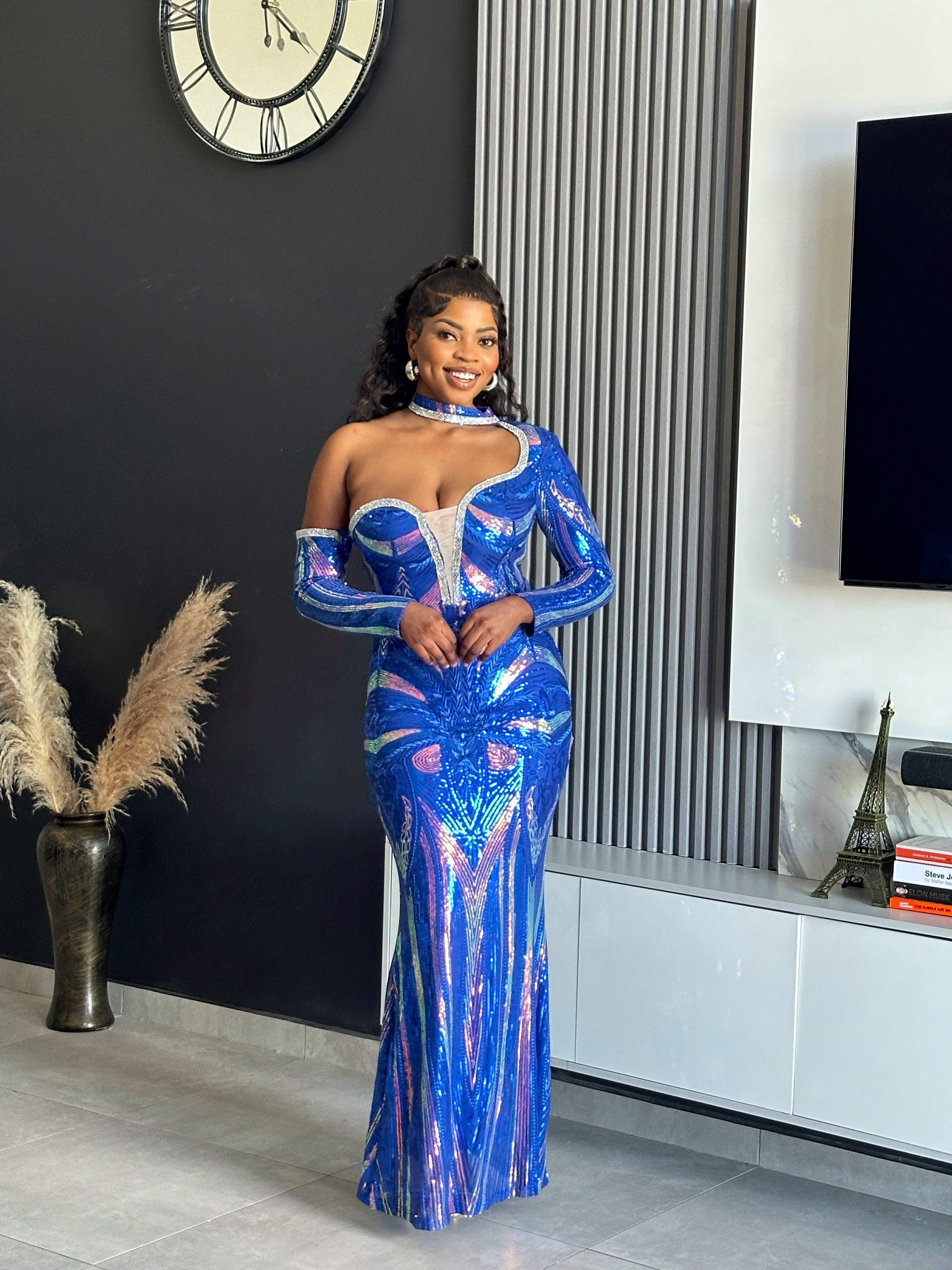 A woman wearing the Glammed Up Shimmering Blue Maxi Dress, featuring off-shoulder sleeves and sparkling details, perfect for elegant occasions