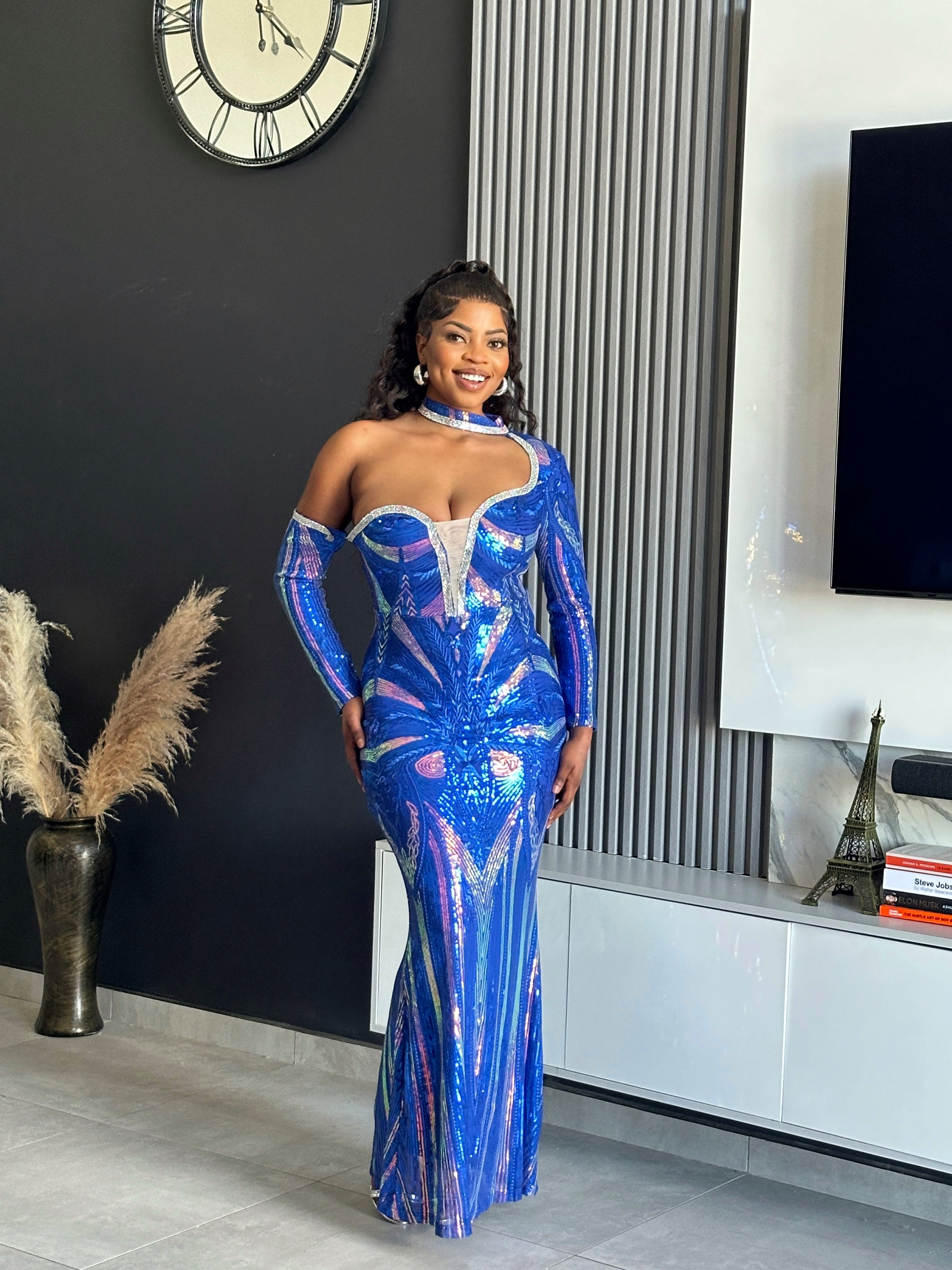 A woman wearing the Glammed Up Shimmering Blue Maxi Dress, featuring off-shoulder sleeves and sparkling details, perfect for elegant occasions