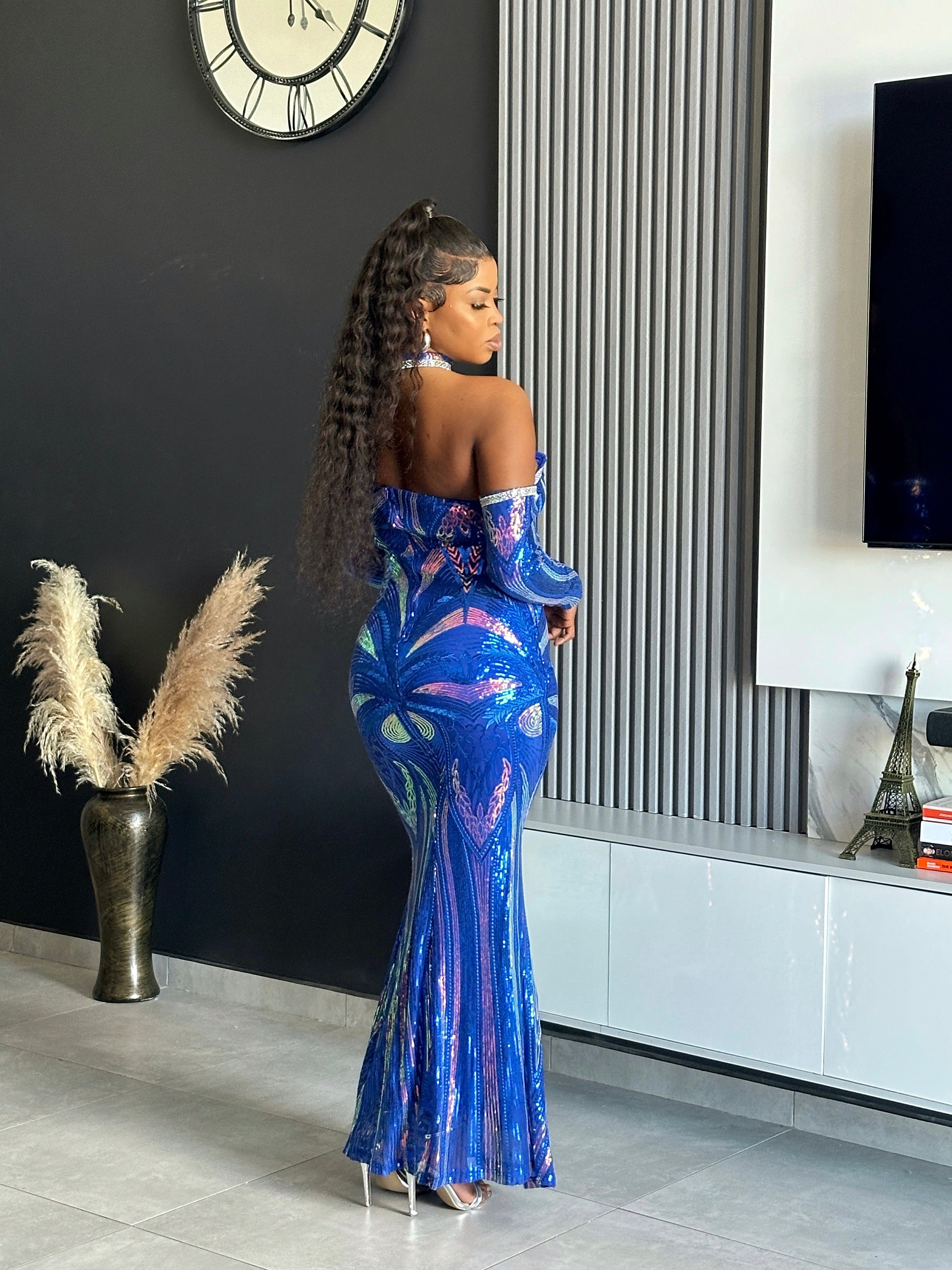 A woman wearing the Glammed Up Shimmering Blue Maxi Dress, featuring off-shoulder sleeves and sparkling details, perfect for elegant occasions