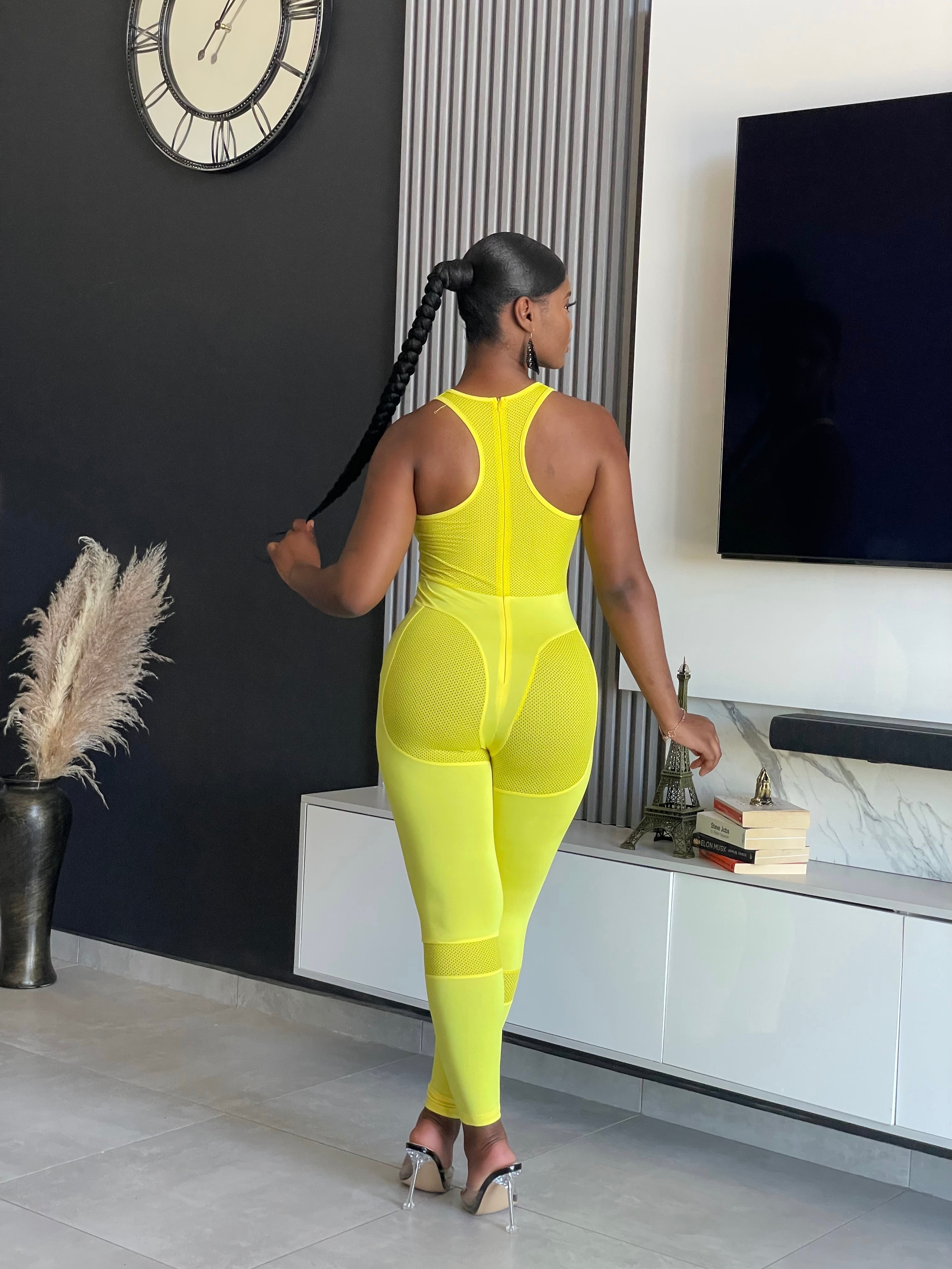 A woman wearing the Say Less Athletic Jumpsuit in neon yellow, featuring mesh panels and a form-fitting design, ideal for fitness enthusiasts seeking style and function.