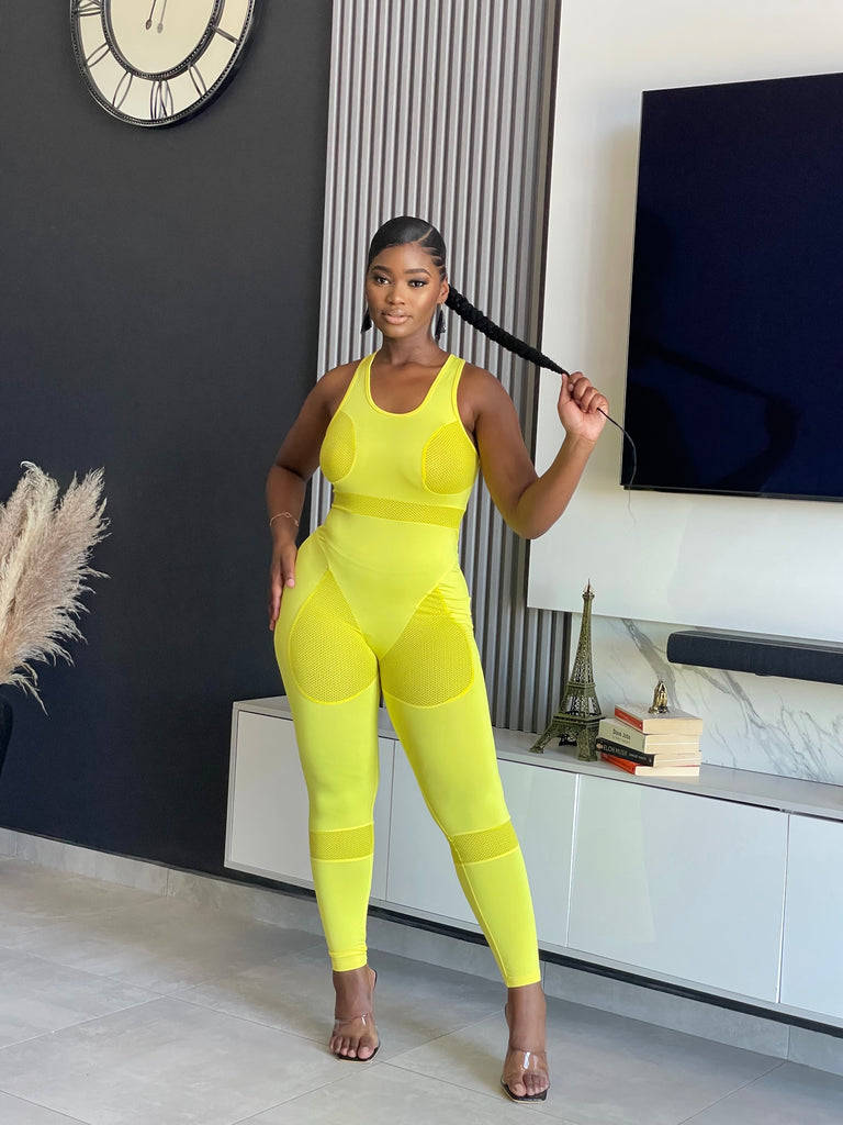 A woman wearing the Say Less Athletic Jumpsuit in neon yellow, featuring mesh panels and a form-fitting design, ideal for fitness enthusiasts seeking style and function.