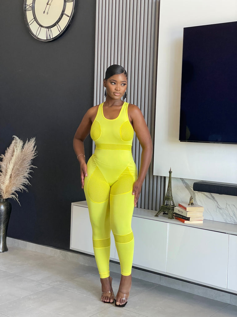 A woman wearing the Say Less Athletic Jumpsuit in neon yellow, featuring mesh panels and a form-fitting design, ideal for fitness enthusiasts seeking style and function.