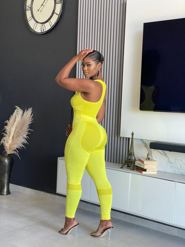 A woman wearing the Say Less Athletic Jumpsuit in neon yellow, featuring mesh panels and a form-fitting design, ideal for fitness enthusiasts seeking style and function.