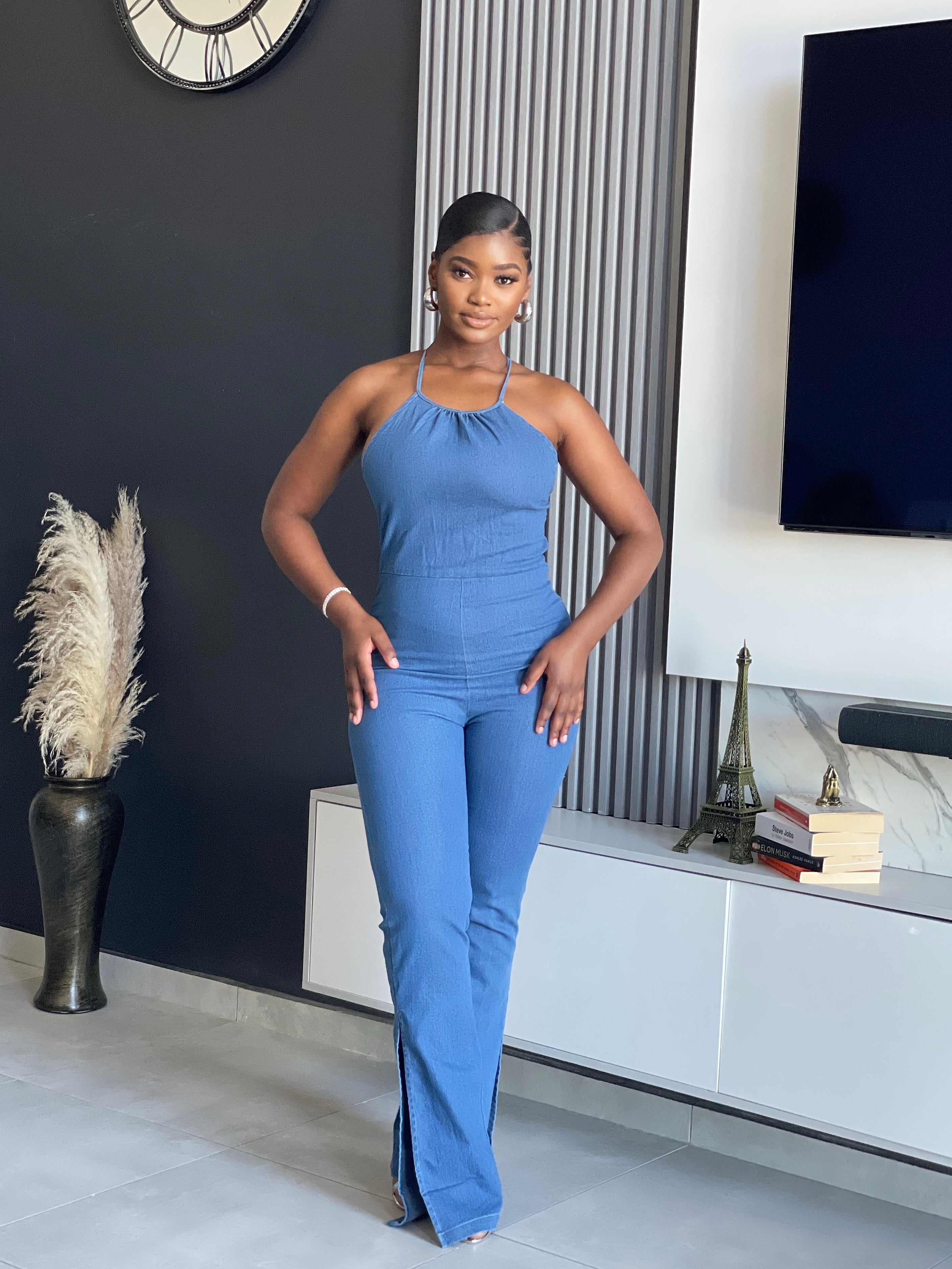 A woman wearing the ‘ SetThe Trend Denim Jumpsuit’ with a halter top and flared legs, showcasing a stretchy, comfortable fit, ideal for fashionable outings.