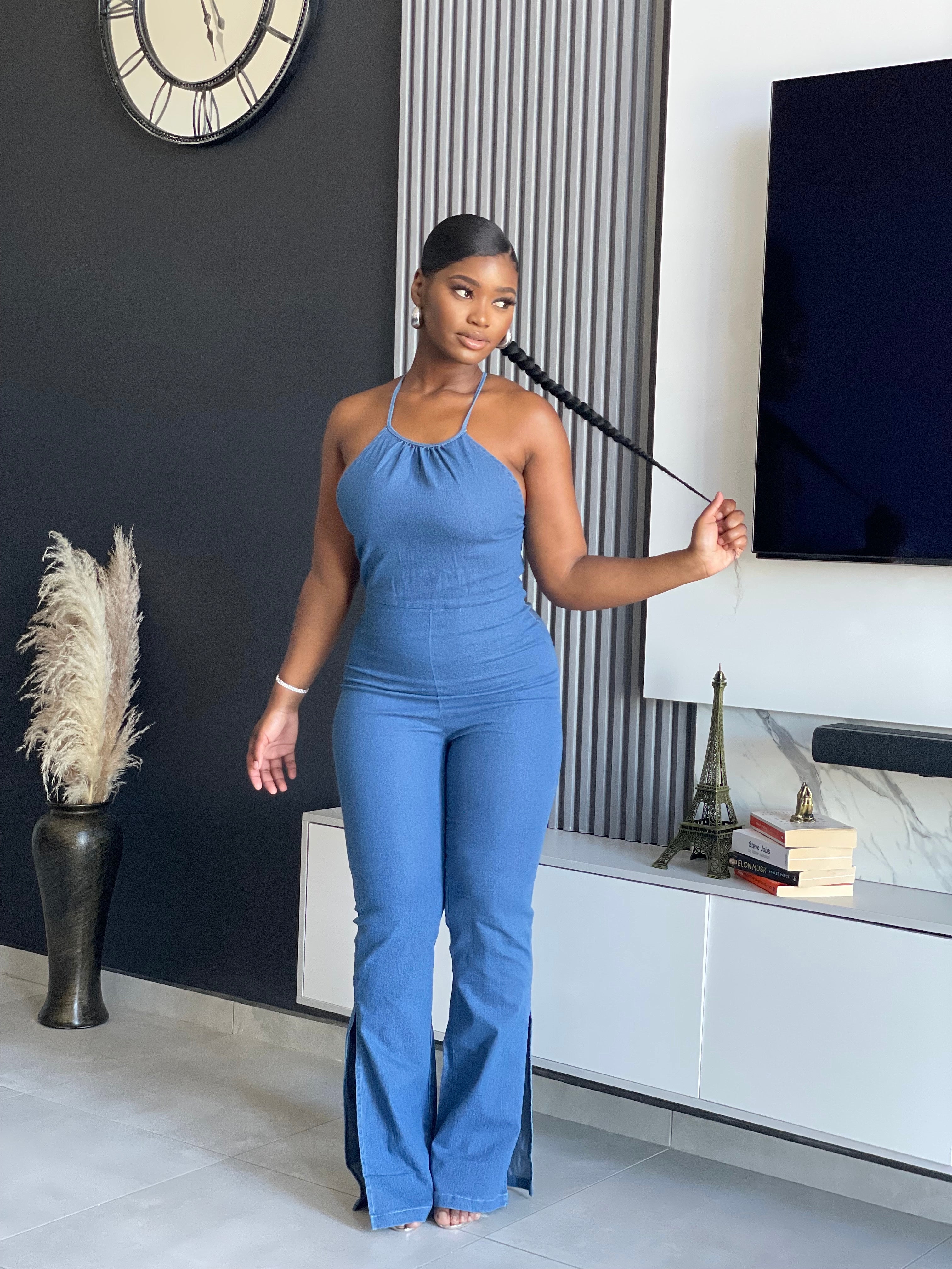 A woman wearing the ‘ SetThe Trend Denim Jumpsuit’ with a halter top and flared legs, showcasing a stretchy, comfortable fit, ideal for fashionable outings.