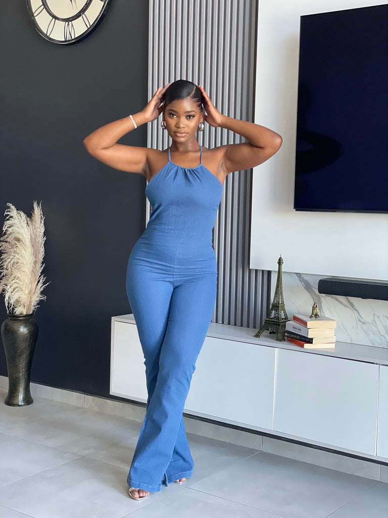 A woman wearing the ‘ SetThe Trend Denim Jumpsuit’ with a halter top and flared legs, showcasing a stretchy, comfortable fit, ideal for fashionable outings.