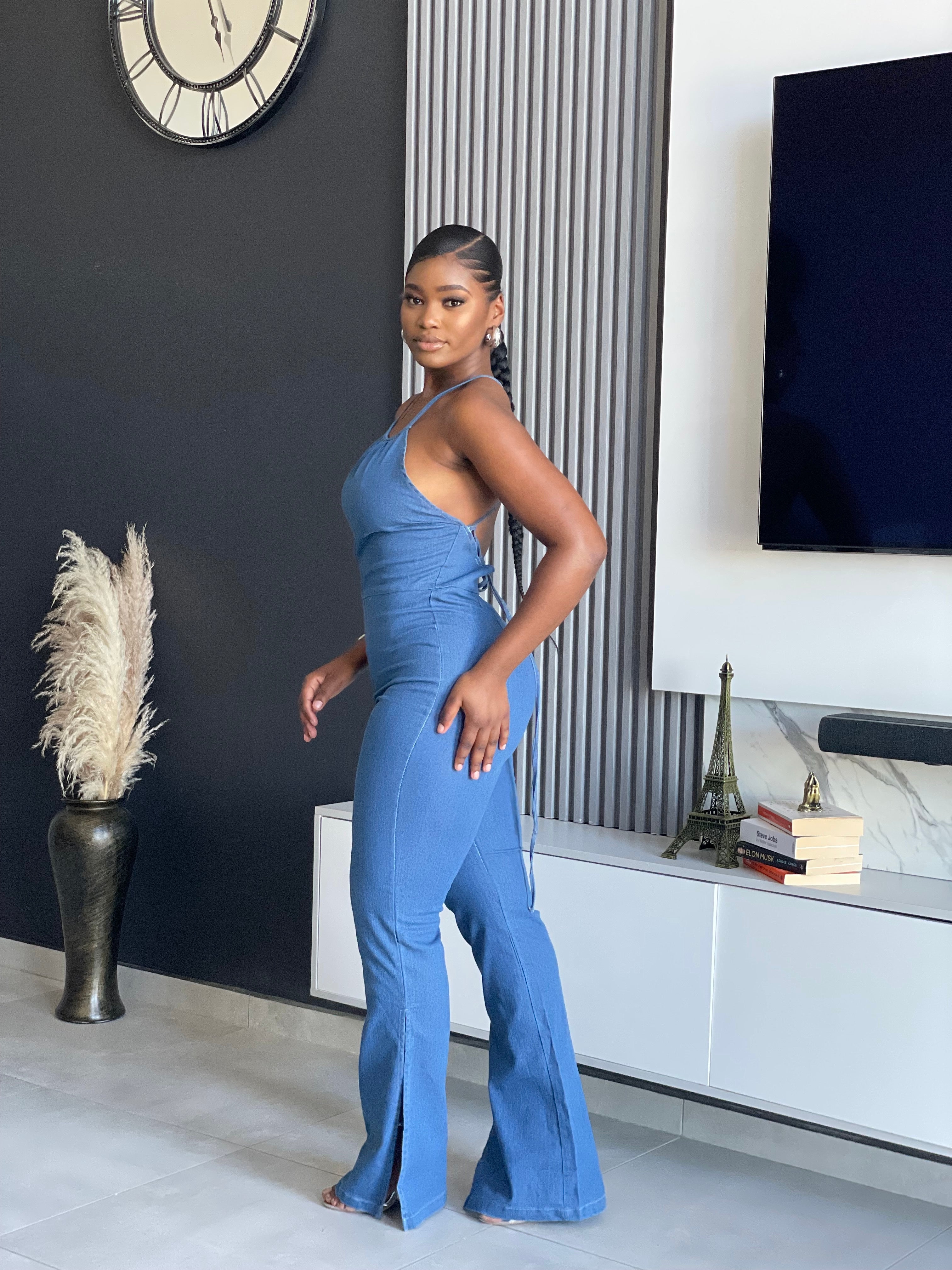 A woman wearing the ‘ SetThe Trend Denim Jumpsuit’ with a halter top and flared legs, showcasing a stretchy, comfortable fit, ideal for fashionable outings.