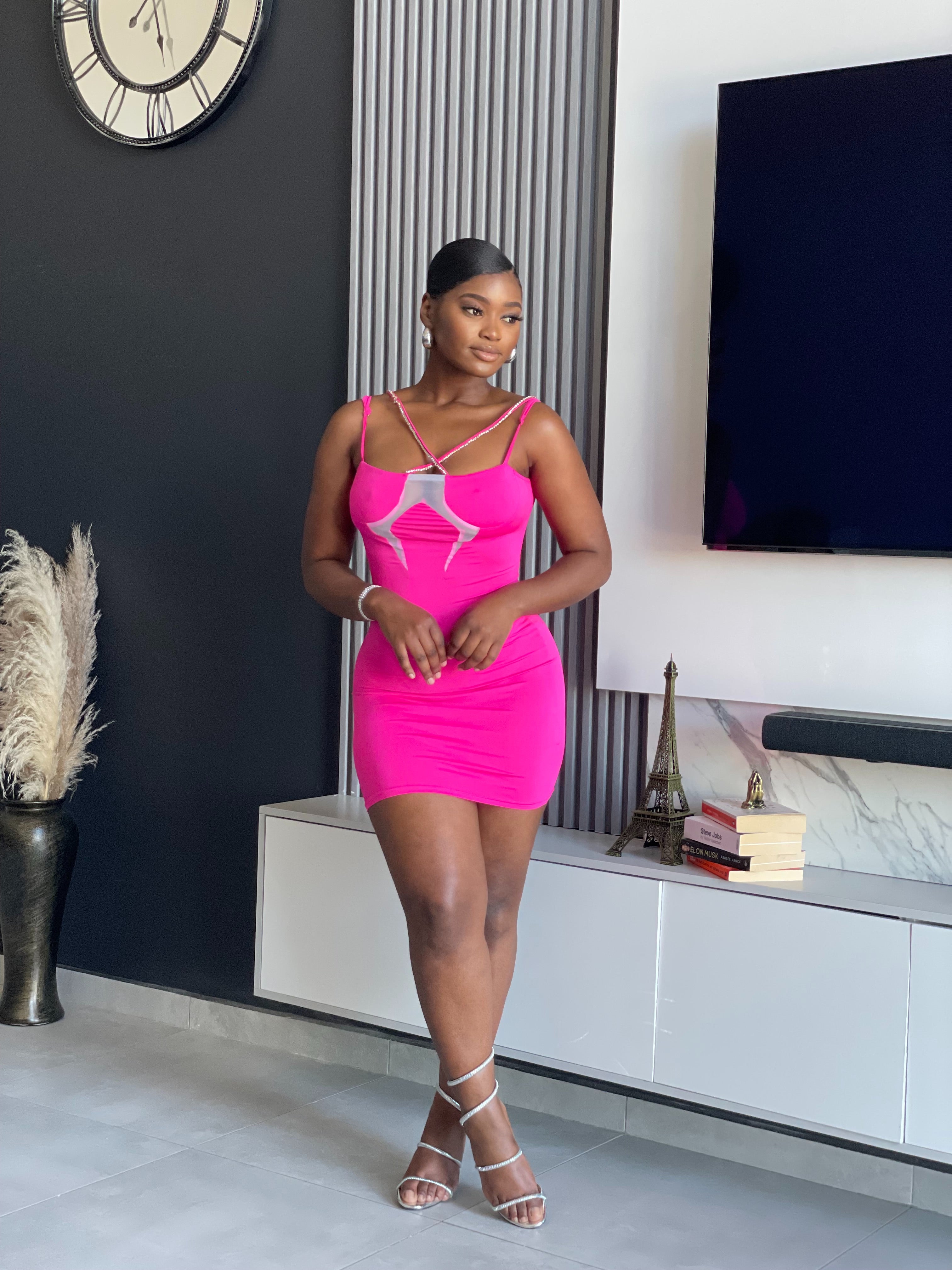 A woman wearing the Sace Bodycon Mini Dress in vibrant pink, perfect for enhancing your party wardrobe with its unique strap details and snug fit.