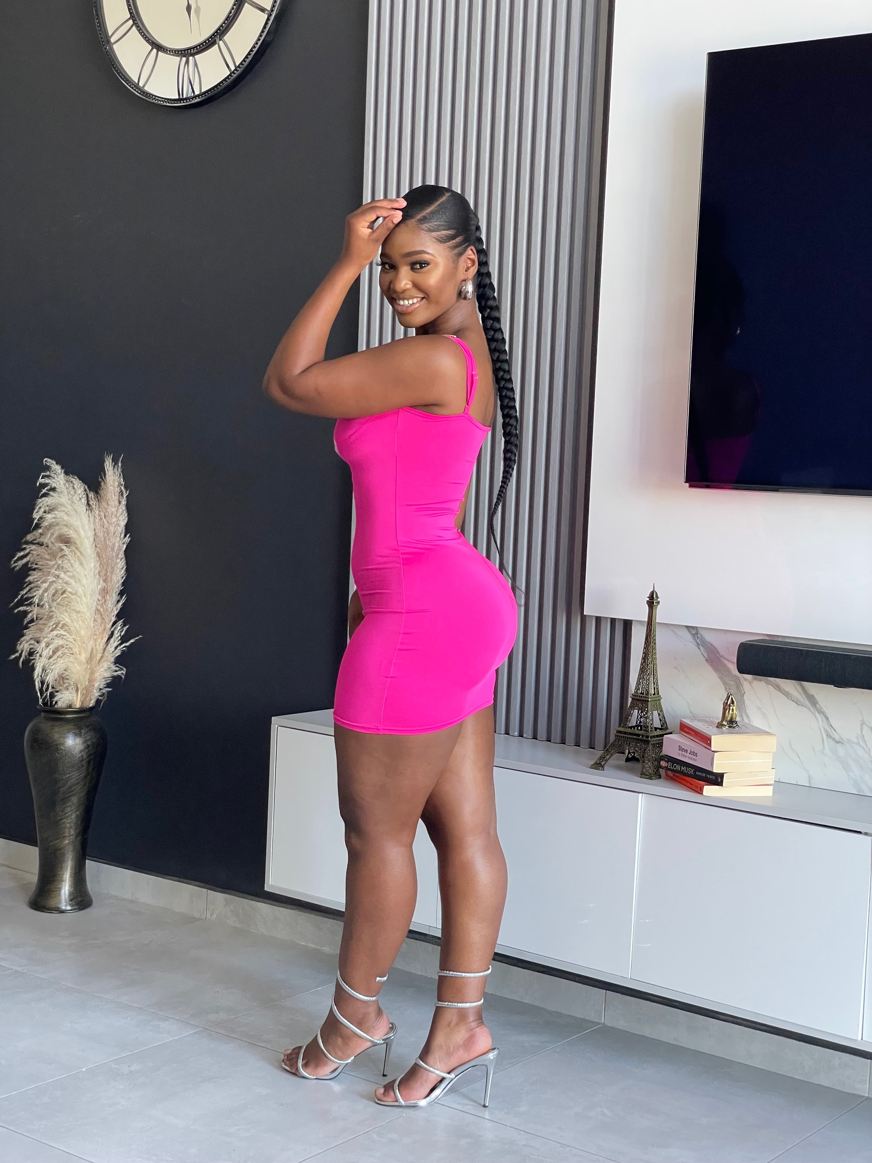 A woman wearing the Sace Bodycon Mini Dress in vibrant pink, perfect for enhancing your party wardrobe with its unique strap details and snug fit.