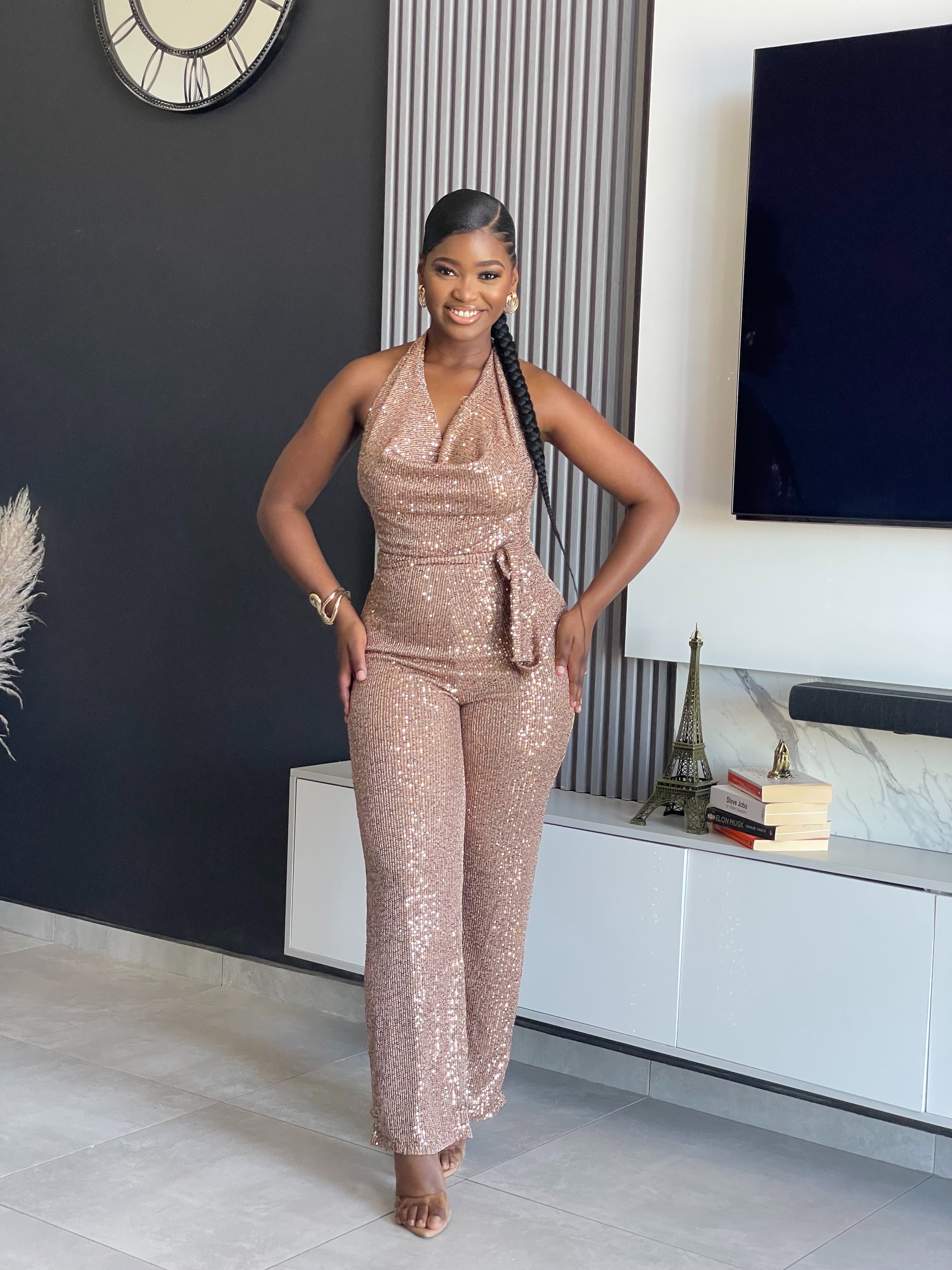 A woman wearing the Bday Sparkle Sequin Jumpsuit, a glamorous sequin-embellished outfit with a halter neckline and belted waist, perfect for special celebrations.