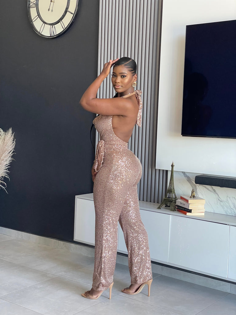 A woman wearing the Bday Sparkle Sequin Jumpsuit, a glamorous sequin-embellished outfit with a halter neckline and belted waist, perfect for special celebrations.