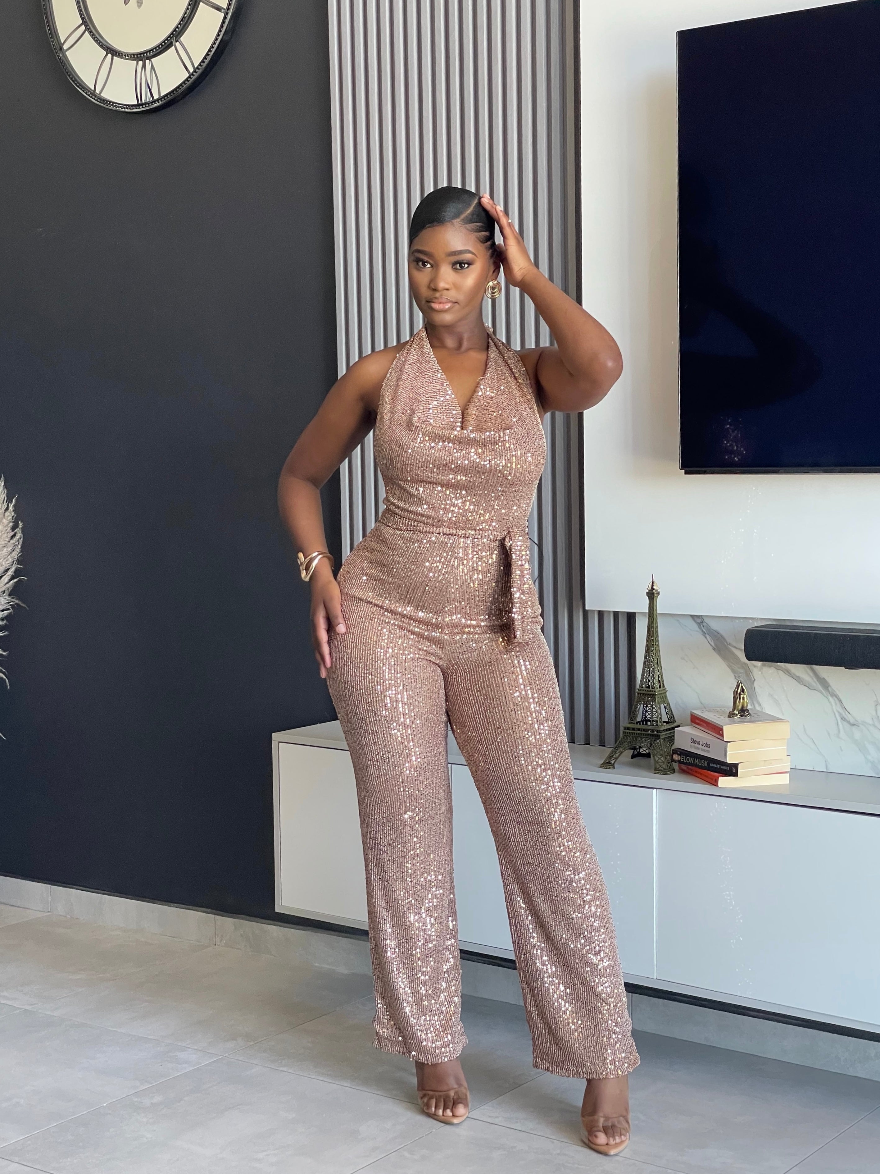 A woman wearing the Bday Sparkle Sequin Jumpsuit, a glamorous sequin-embellished outfit with a halter neckline and belted waist, perfect for special celebrations.