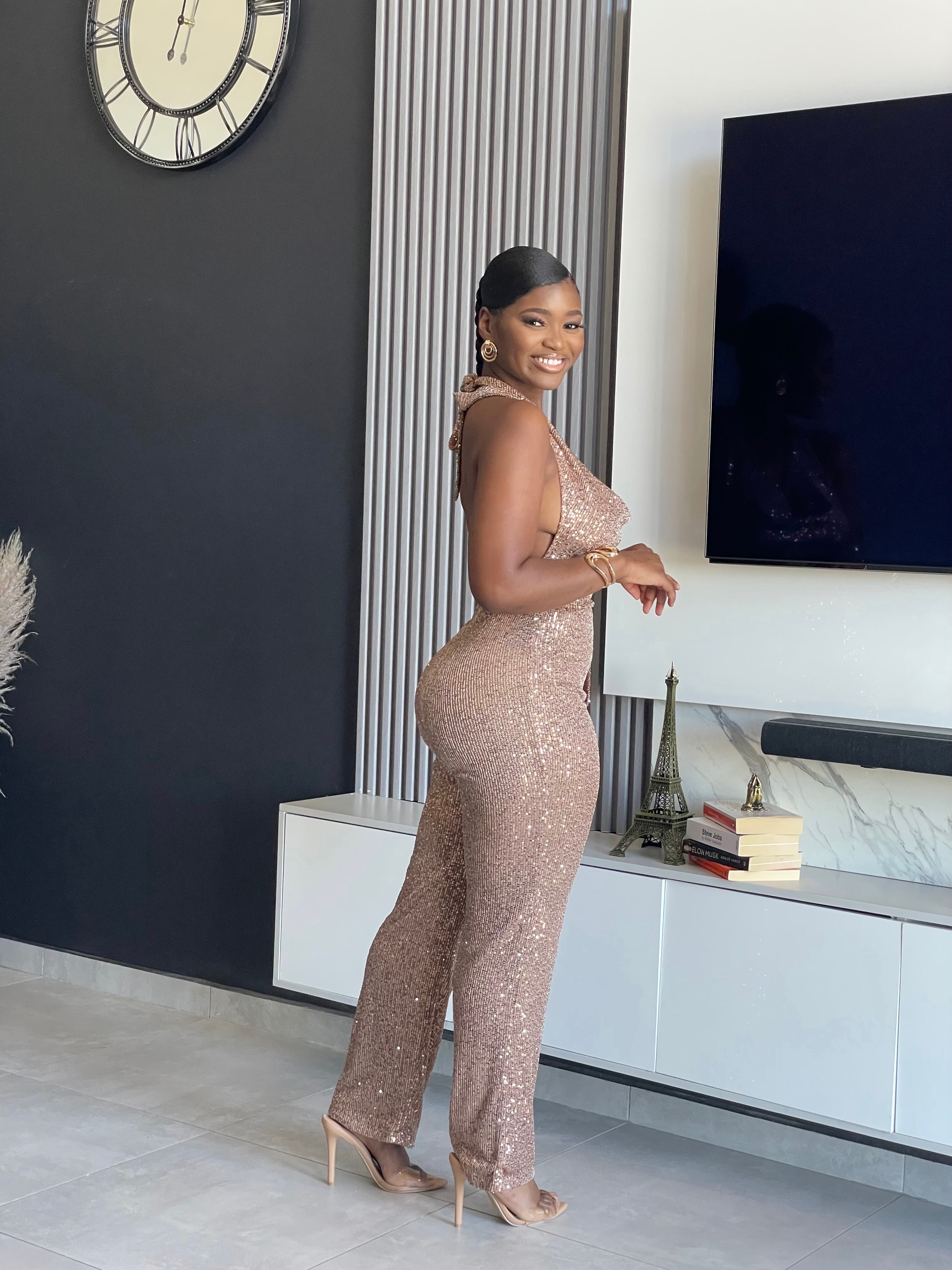 A woman wearing the Bday Sparkle Sequin Jumpsuit, a glamorous sequin-embellished outfit with a halter neckline and belted waist, perfect for special celebrations.