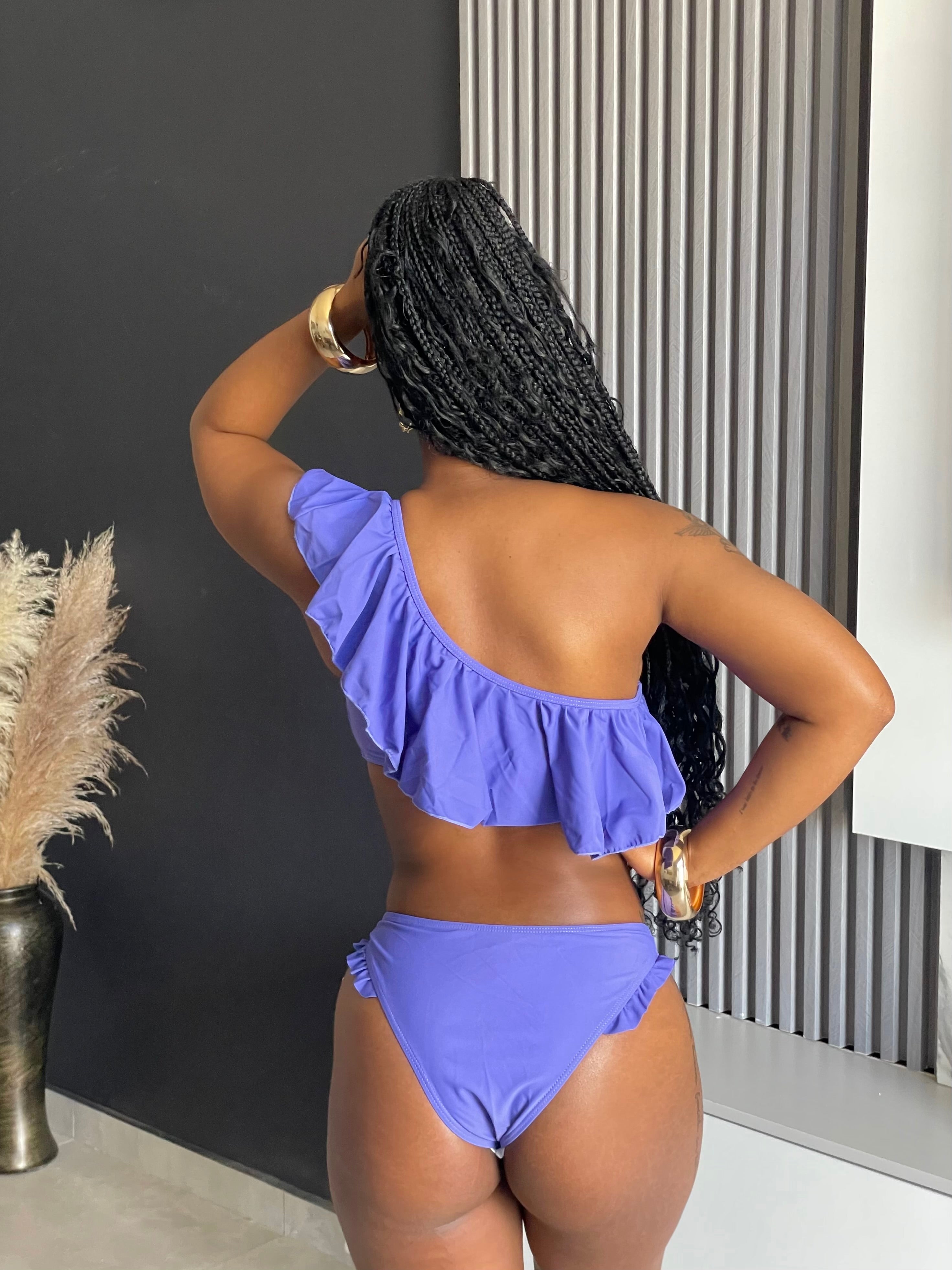 A woman wearing the Cassie Ruffle Bikini in lavender, featuring a ruffle top and classic bottoms, ideal for stylish beach and pool days.