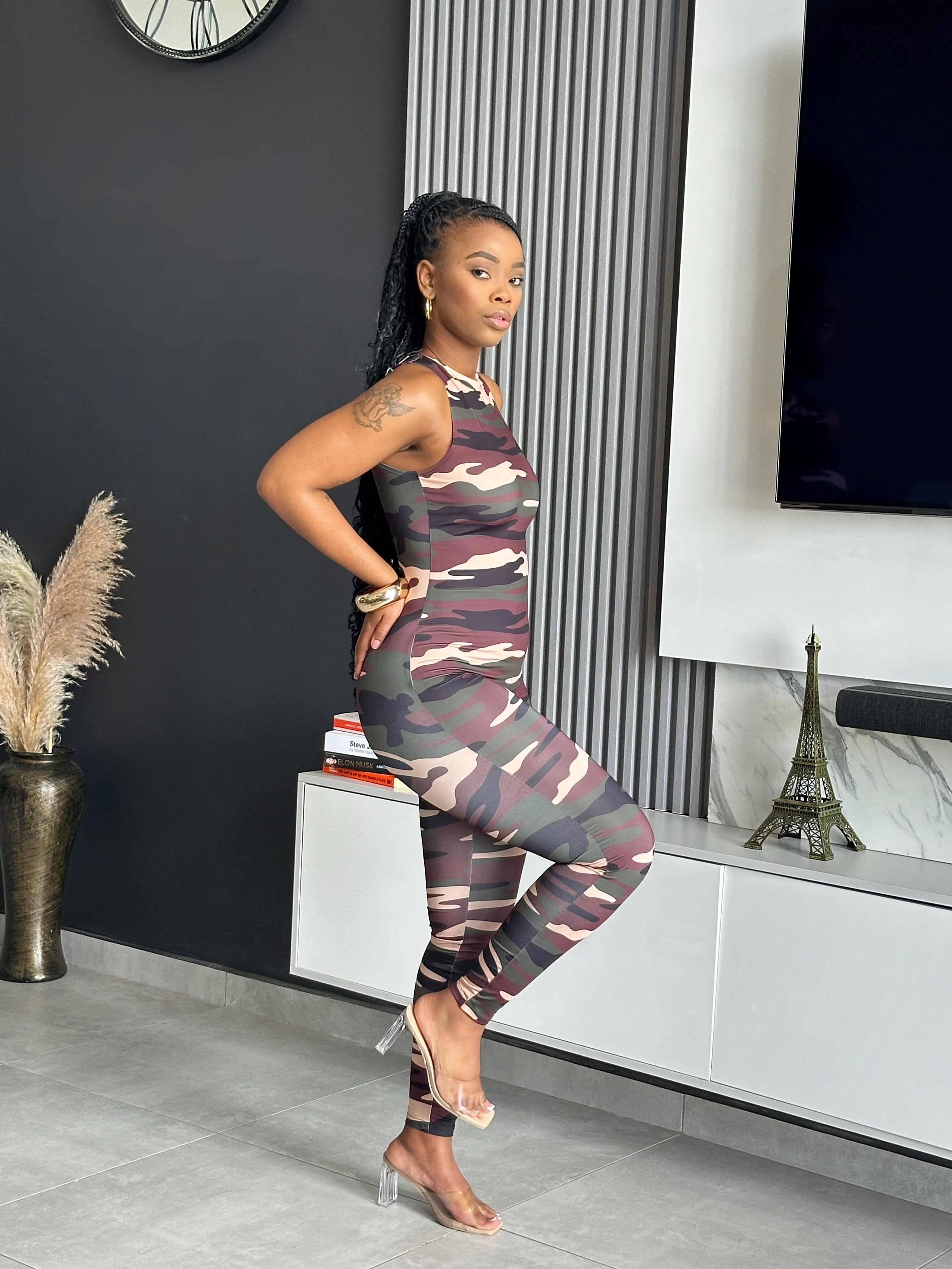 Model wearing the Nedia Jumpsuit, a camo print one-piece with a sleeveless design and form-fitting silhouette